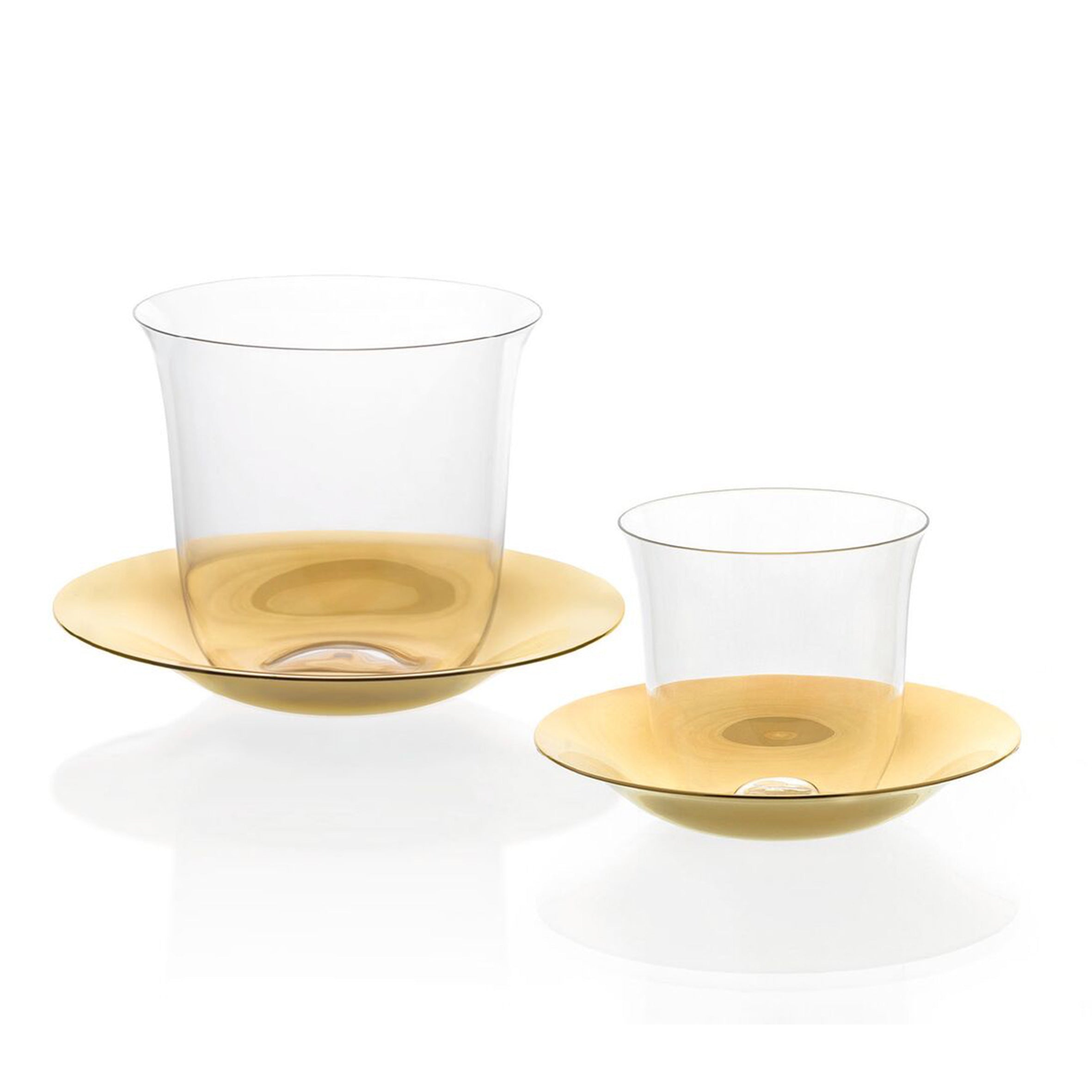 The Lily Mokka Set by Lobmeyr features two transparent crystal glass cups, each on a matching gold-colored saucer, with one cup larger than the other. The reflective surface enhances the sophisticated design against a white background.
