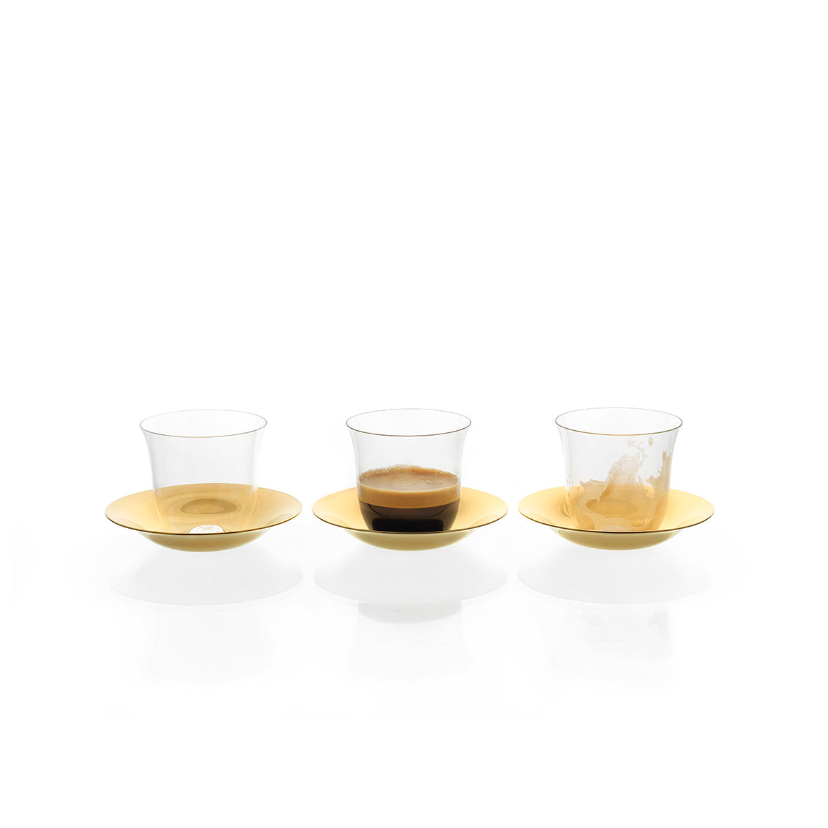 Three clear mouth-blown lead-free crystal Lily Mokka glasses from Lobmeyr rest on gold saucers against a white background. The left glass is empty, the middle has espresso, and the right cup shows coffee stains, suggesting recent use.