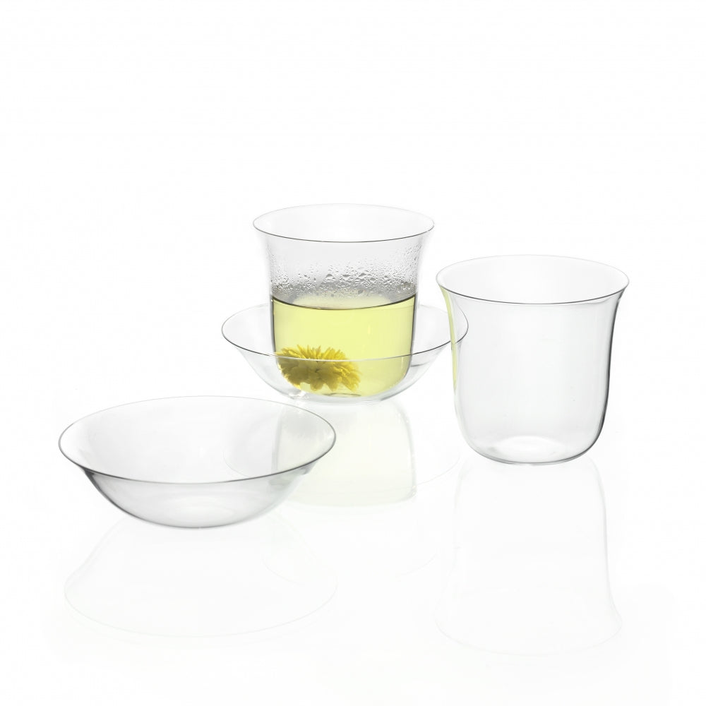 The elegantly arranged Lily Tea Set features a Lobmeyr tea glass, containing a light yellow liquid with a flower inside, while three transparent crystal glass cups and bowls rest empty. This exquisite glassware is beautifully displayed on a reflective white surface.
