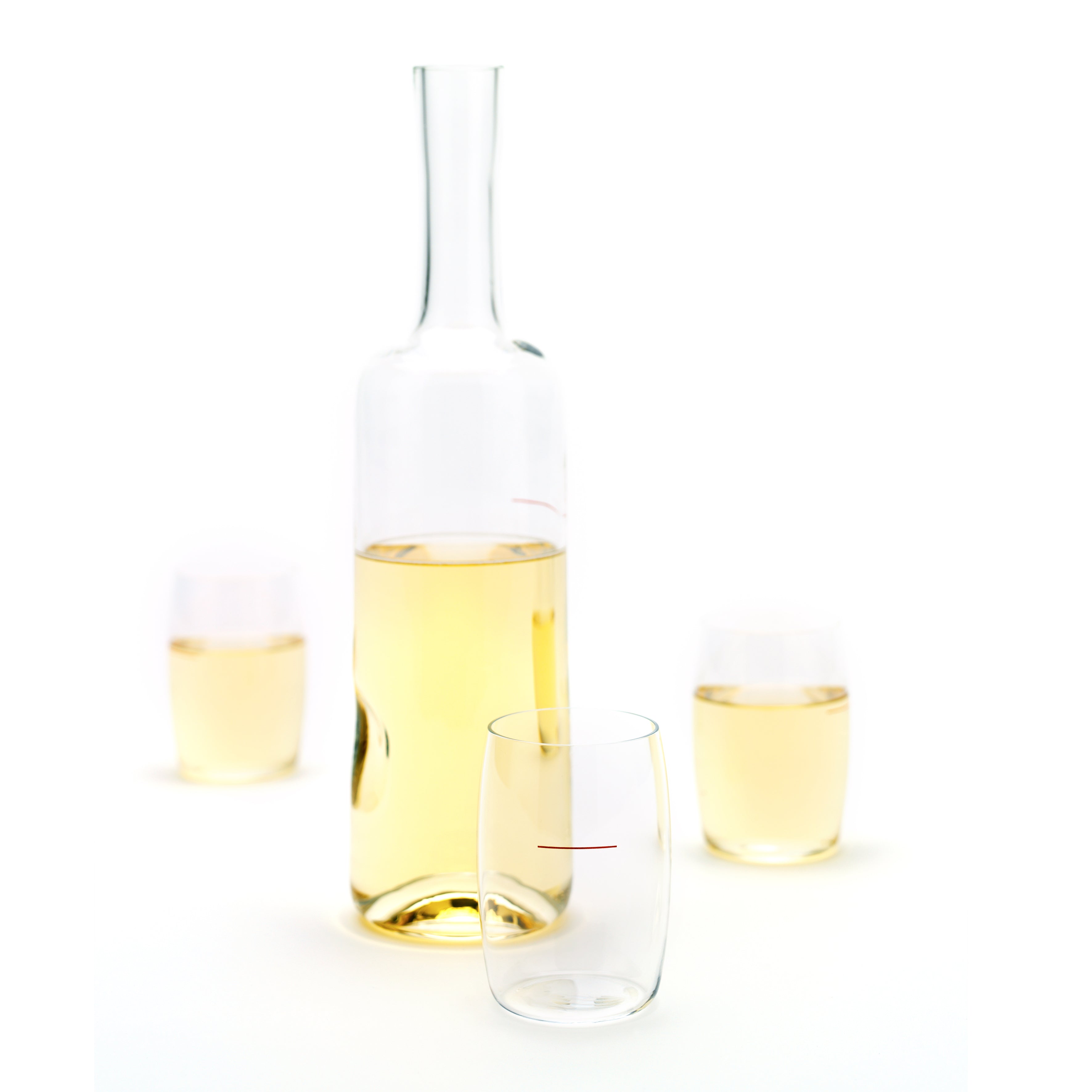 A clear glass carafe with white wine is alongside two filled stemless Mak Achtel glasses, made from lead-free crystal by Lobmeyr. An empty glass with a subtle red design lies elegantly in front, all set against a minimalist white background reflecting Peter Noevers refined style.