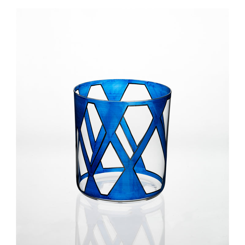 A cylindrical glass from Lobmeyrs Neo Light VIII Enamel Collection features a modern design of interconnected blue triangles and diamonds on a white backdrop, reminiscent of Martino Gampers style, blending contemporary artistry with classic craftsmanship on its transparent surface.