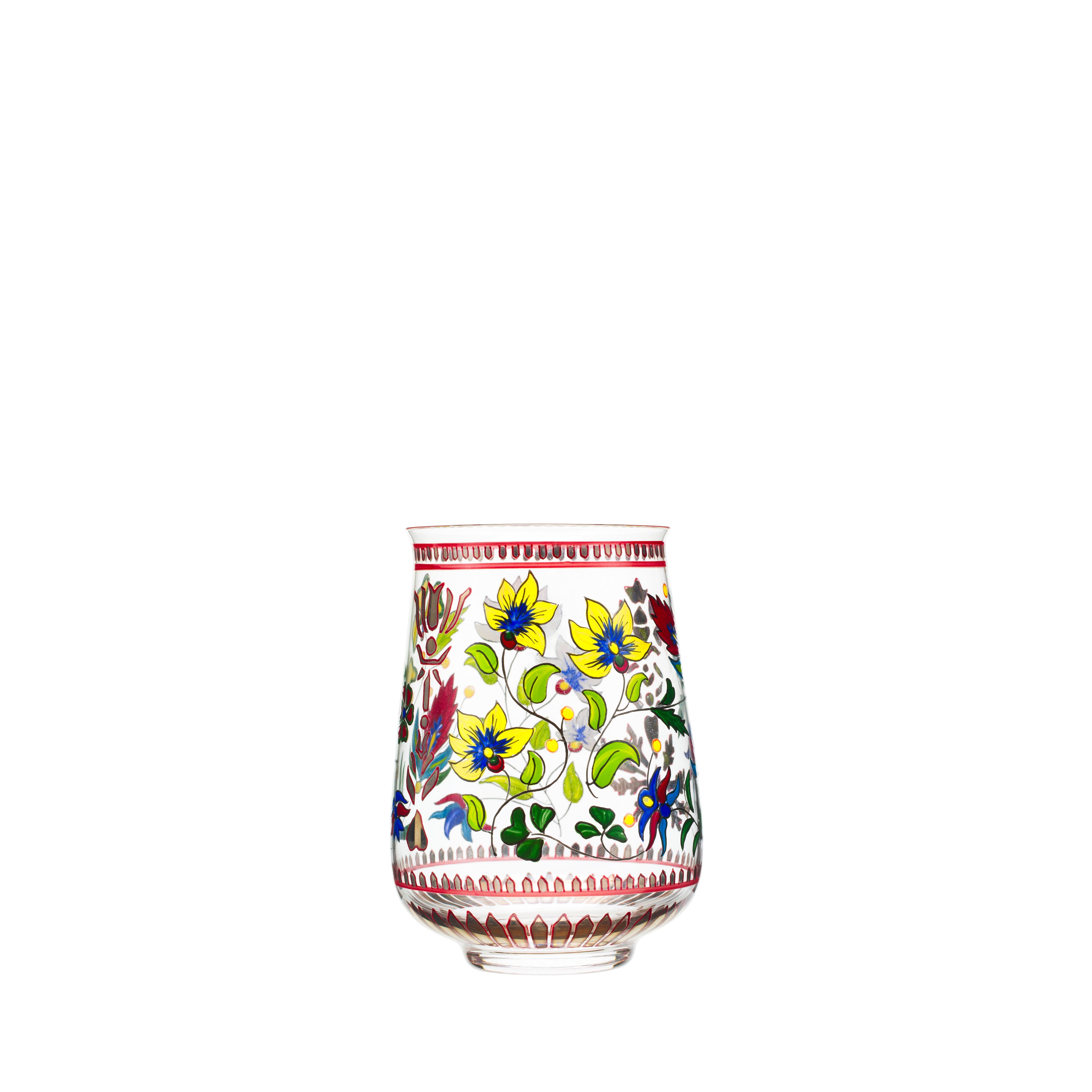 The Oriental Flower Tumbler by Lobmeyr is a transparent glass tumbler with colorful floral motifs featuring yellow, blue, and red flowers with green leaves. It includes a hand-painted crystal border with a red zigzag design around the rim and base.