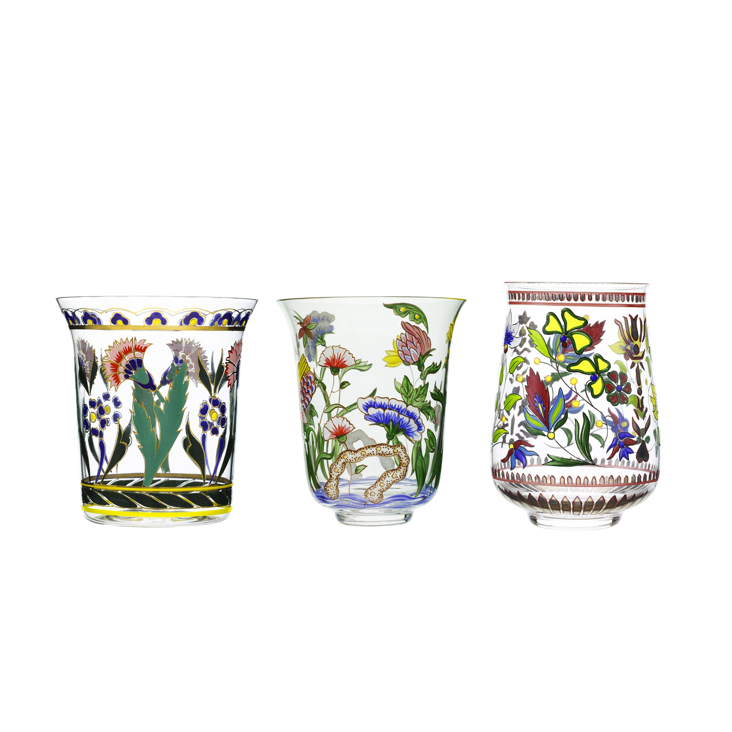 Three Lobmeyr Oriental Flower Tumblers, adorned with intricate colorful floral and botanical patterns, are displayed. The left and right tumblers boast vivid oriental designs in green, red, and yellow, while the middle one has muted tones. All stand against a white background.