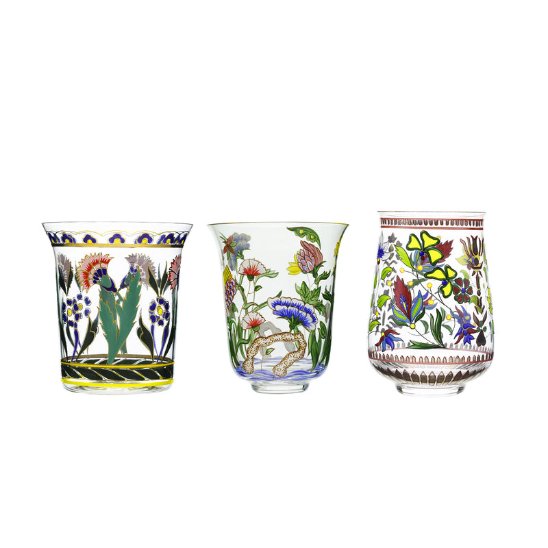 Three Lobmeyr Oriental Flower Tumblers, adorned with intricate colorful floral and botanical patterns, are displayed. The left and right tumblers boast vivid oriental designs in green, red, and yellow, while the middle one has muted tones. All stand against a white background.