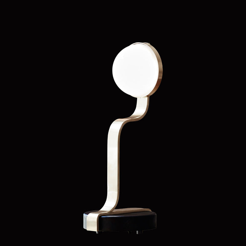 The Script Table Lamp by Lobmeyr features a modern, minimalist design with a curved metallic stand and round white shade atop. Its sleek base complements the style, and LED lighting provides a gentle glow, all set against a black background.
