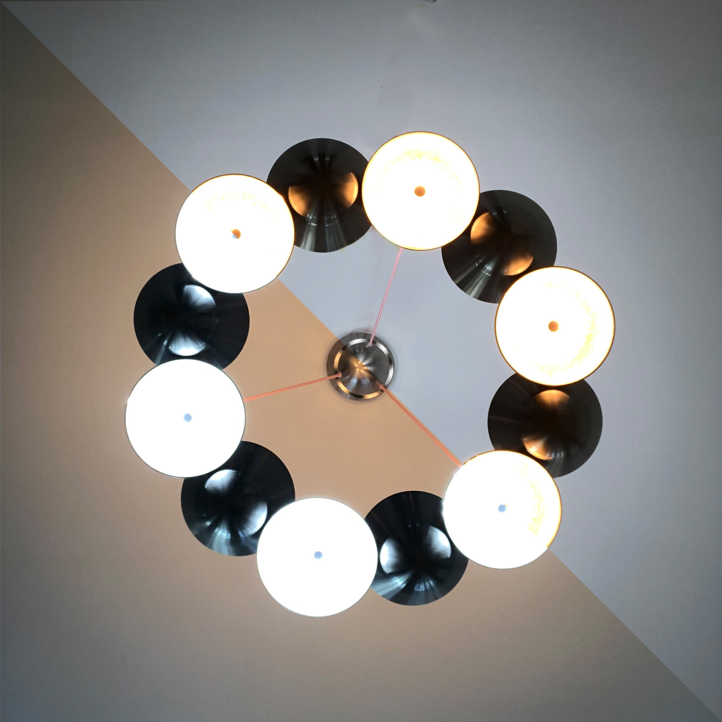 The Knight 12 by Lobmeyr is a smart chandelier featuring eight circular lights in a ring, alternating warm and cool tones around a central metal fixture. It complements a two-tone ceiling with intersecting lines, embodying modern sophistication inspired by Lobmeyr design.
