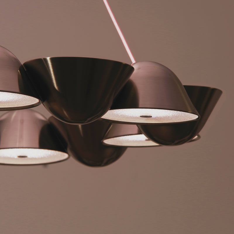 The Lobmeyr The Knight 12 is a modern pendant light featuring multiple cone-shaped metallic shades, offering evenly spaced, warm lights that create a contemporary and elegant ambiance similar to that of a classic chandelier.