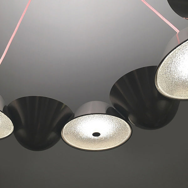 Close-up of The Knight 12 by Lobmeyr, a modern modular lighting fixture with circular lamps and textured glass surfaces, each backed by black funnels. It resembles a Lobmeyr chandelier and is suspended by thin red wires against a gray ceiling.
