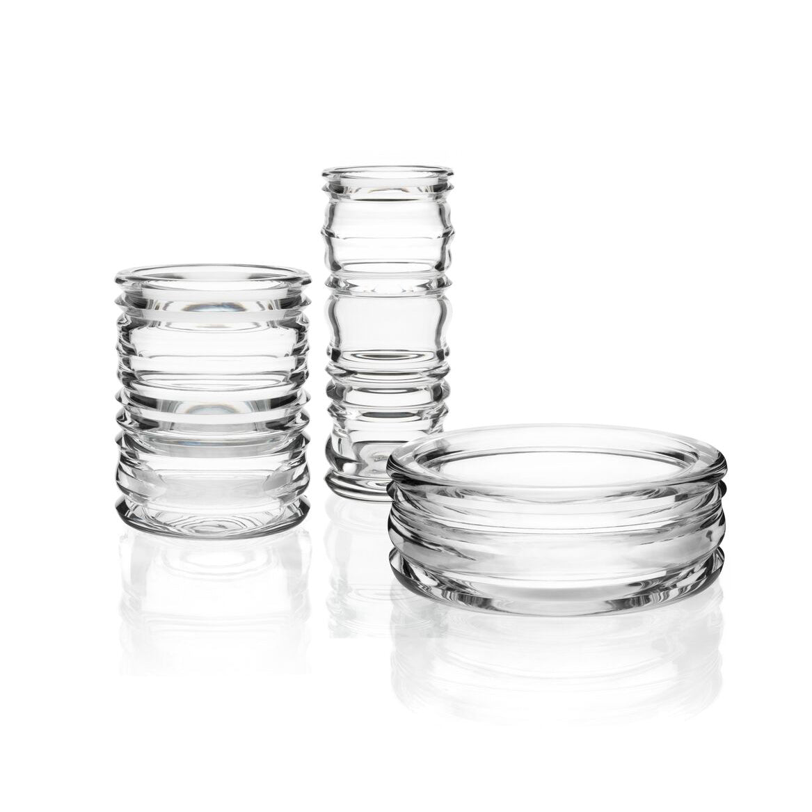 The Thom Series by Lobmeyr features clear, cylindrical glass containers with varying heights and ridged patterns, reflecting light on a white surface and evoking the artistry of mouth-blown glass reminiscent of Sebastian Menschhorns exquisite creations.
