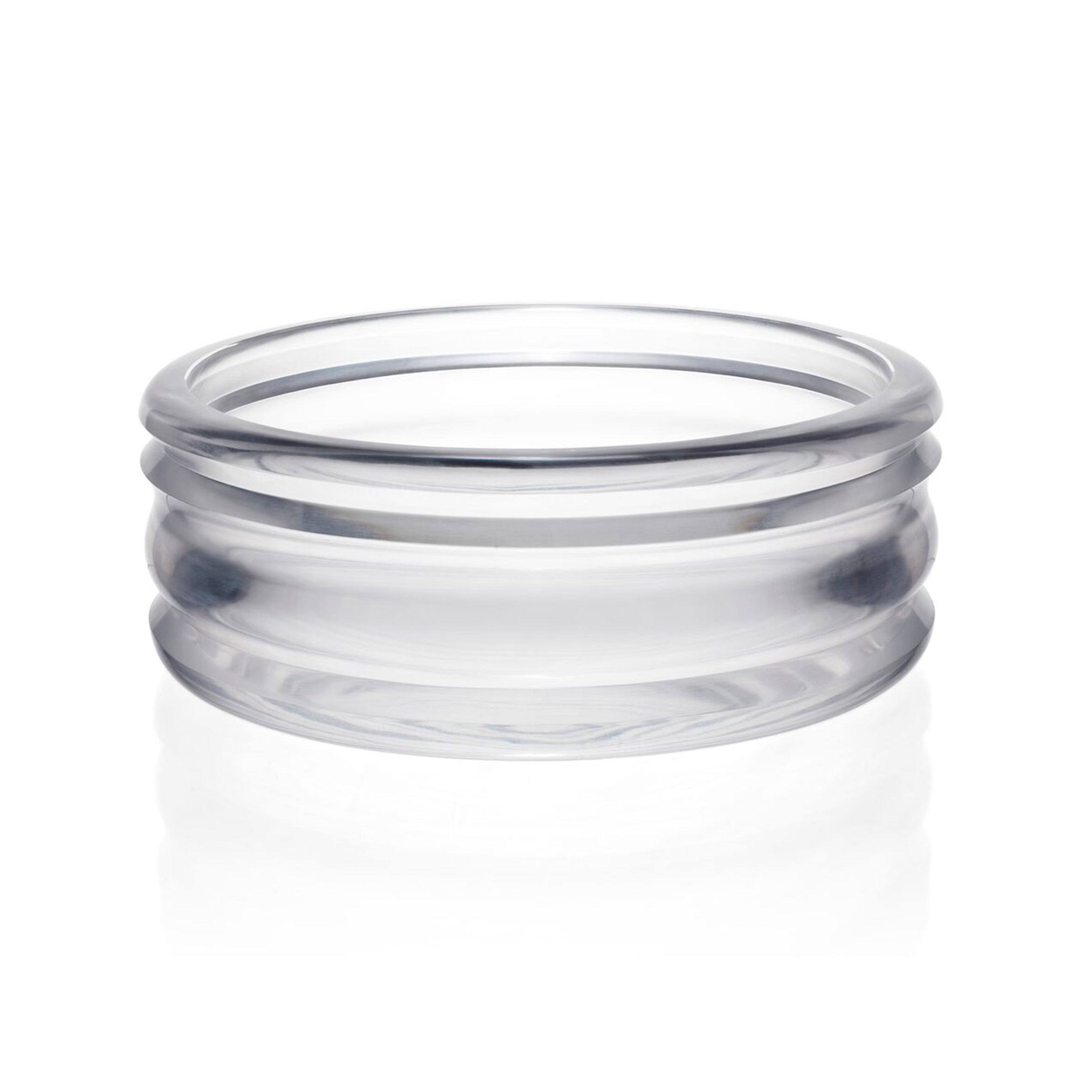 The Thom Series by Lobmeyr features a clear glass bowl with a smooth, stackable design and three rounded ridges. Crafted from mouth-blown glass, it rests on reflective surfaces, highlighting its transparent and minimalist appearance.