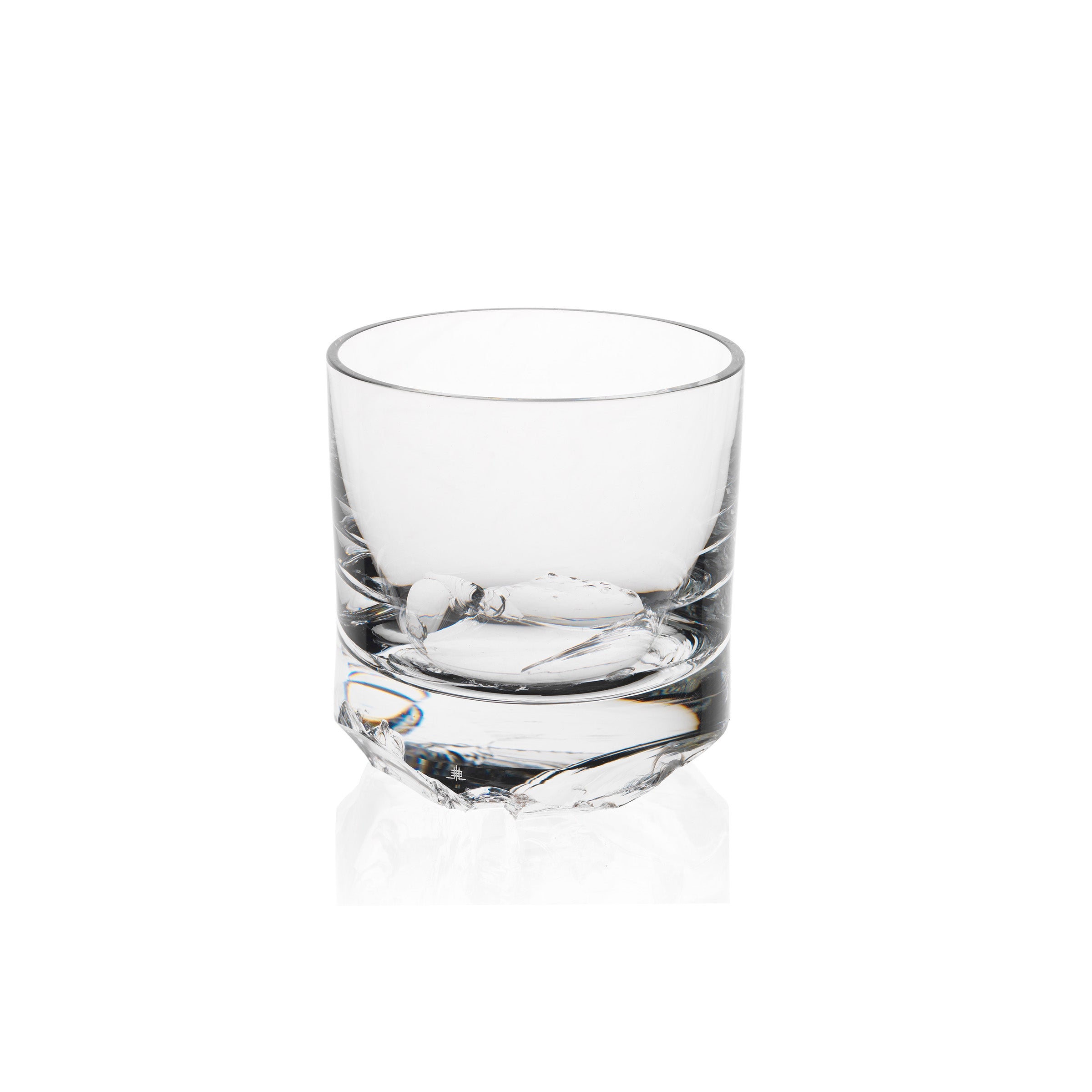 A clear, empty glass with a thick base sits on a plain white background. Its design echoes Michael Anastassiadess style, featuring subtle geometric texture near the bottom, giving a modern touch to the classic Flint tumbler shape from Lobmeyrs Bar Series.