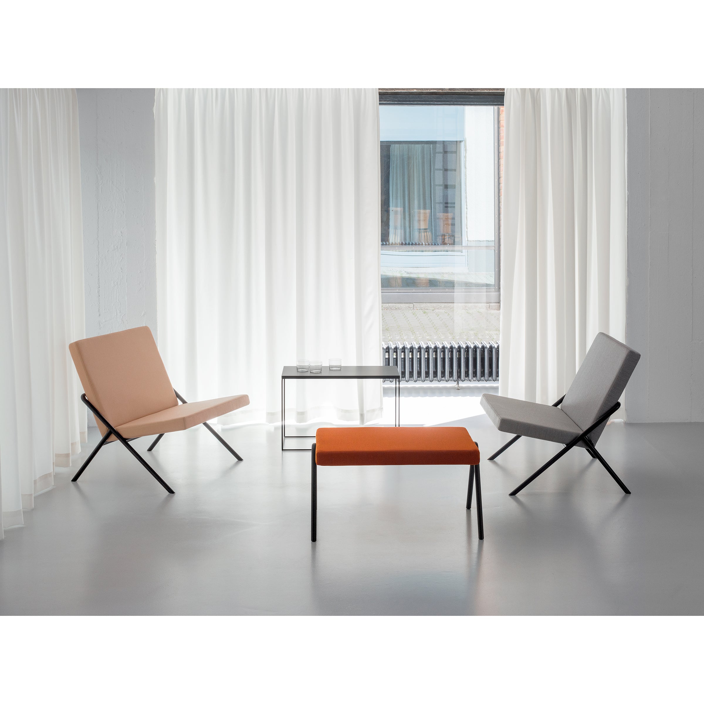 A minimalist room showcases Loehrs DL2 Euclides Lounge Chairs in beige and gray, facing each other. An orange bench centers the design with a small glass table. A large window, white curtains, a light gray floor, and pale walls heighten the serene ambiance.