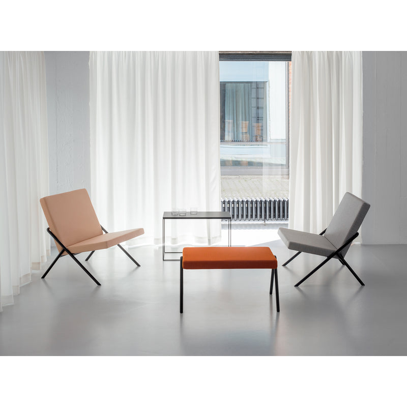 A minimalist room showcases Loehrs DL2 Euclides Lounge Chairs in beige and gray, facing each other. An orange bench centers the design with a small glass table. A large window, white curtains, a light gray floor, and pale walls heighten the serene ambiance.