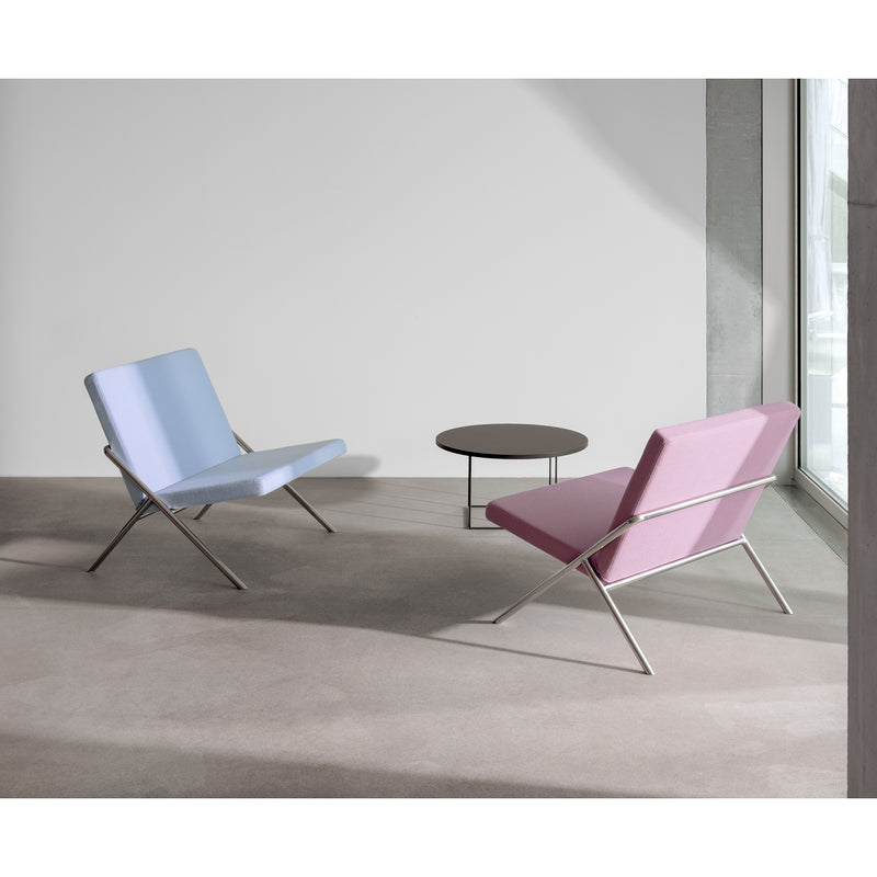 Two DL2 Euclides Lounge Chairs by Loehr, one light blue and one light pink with sleek metal frames, provide elegant seating in a minimalist room. A small round coffee table sits between them on a neutral-toned carpet while large windows fill the space with natural light.