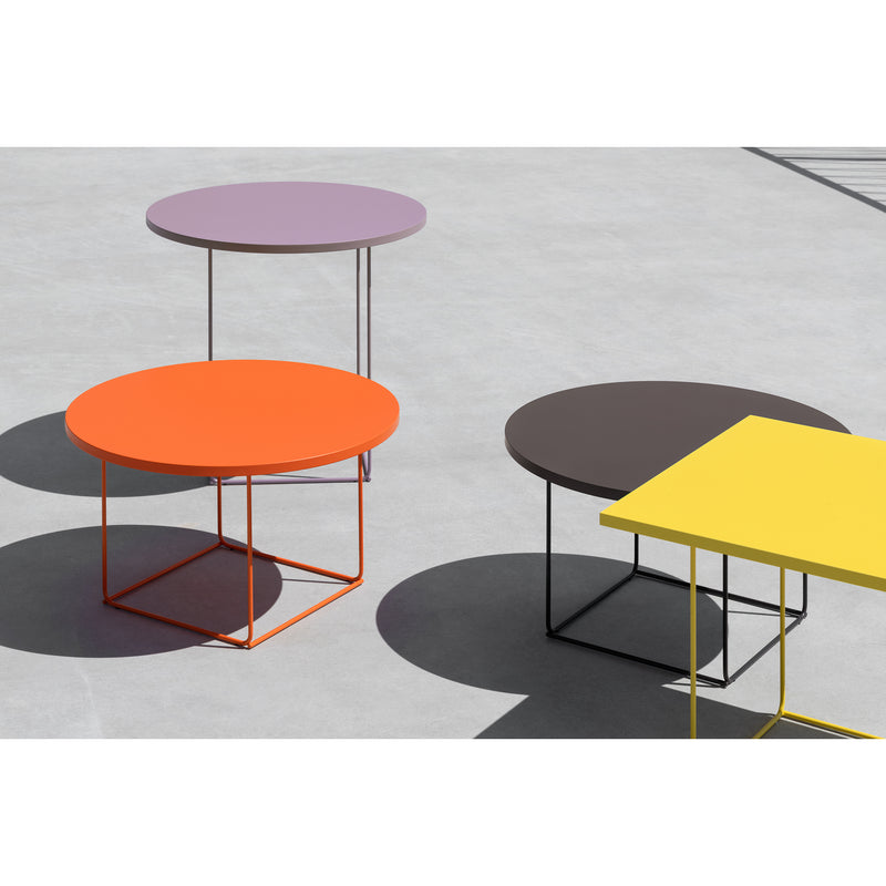 Three DL3 Umbra Tables by Loehr, featuring round tops in purple, orange, and brown with thin metal legs, sit on a concrete surface. Their shadows form distinct tangram-like shapes.