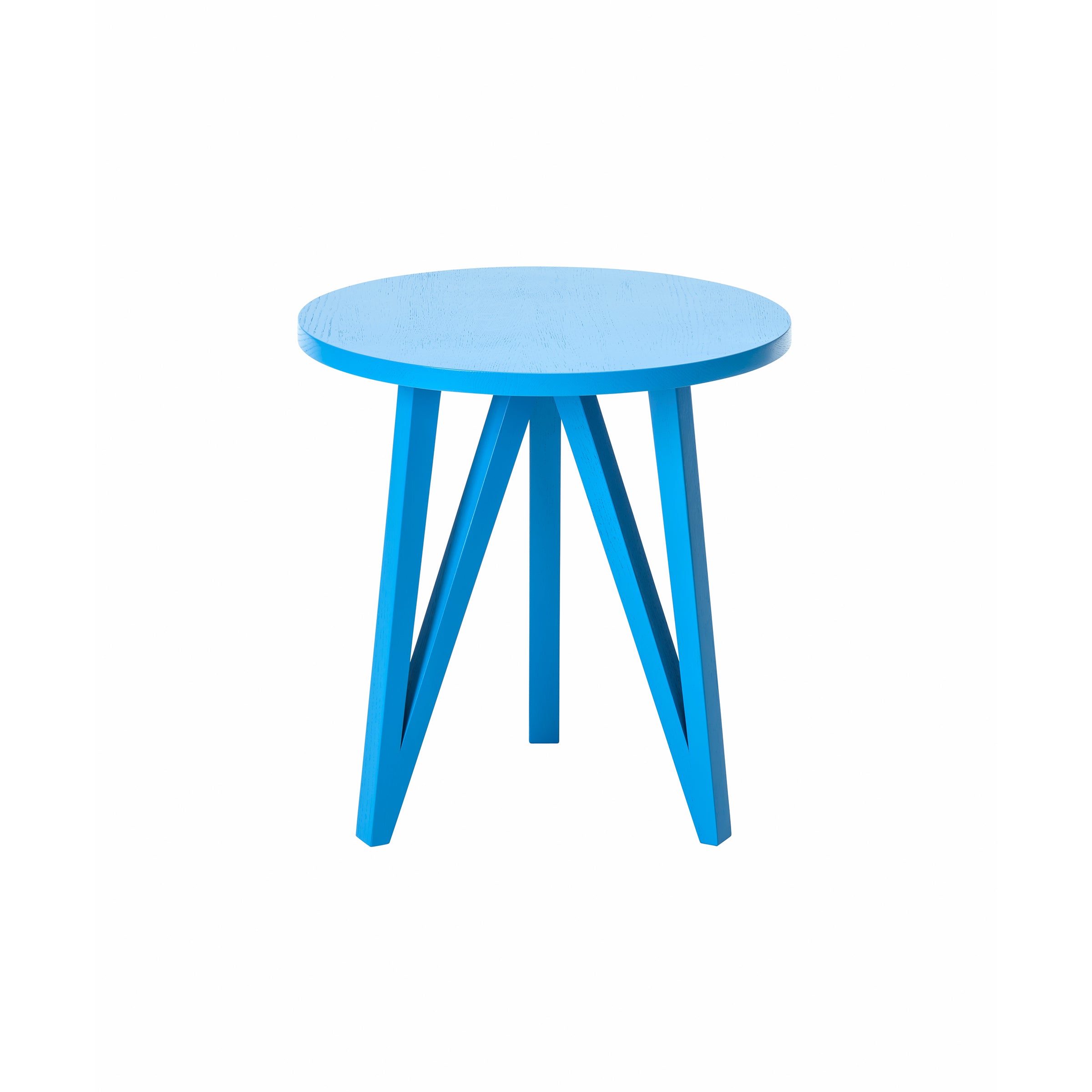 The JL2 Faber Side Table by Loehr is a small, round, blue, wooden table with minimalist design and a unique silhouette. Its smooth top and four angled legs converge at the center. The vibrant color and simple structure, set against a white background, evoke northern European architecture.