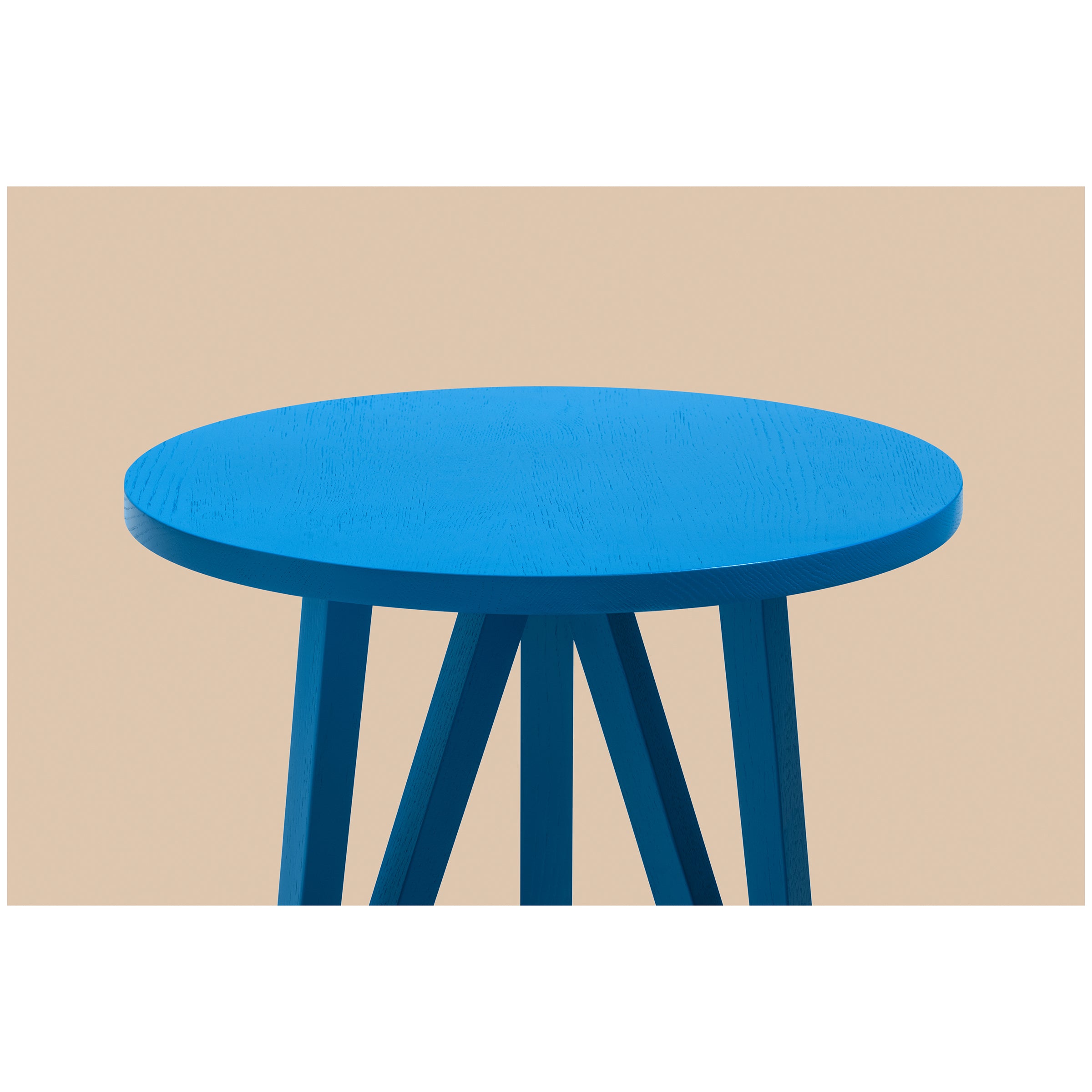 Loehrs JL2 Faber Side Table features a blue round top and angled wooden legs, crafted from solid oak, showcased against a beige background.