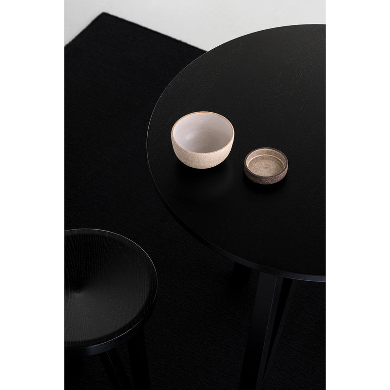 The JL3 Faber Bistro Table by Loehr features a black round tabletop with two bowls—one large white and one small brown—paired with a black stool. This northern European design setup is minimalistic, enhanced by a sleek black carpet.