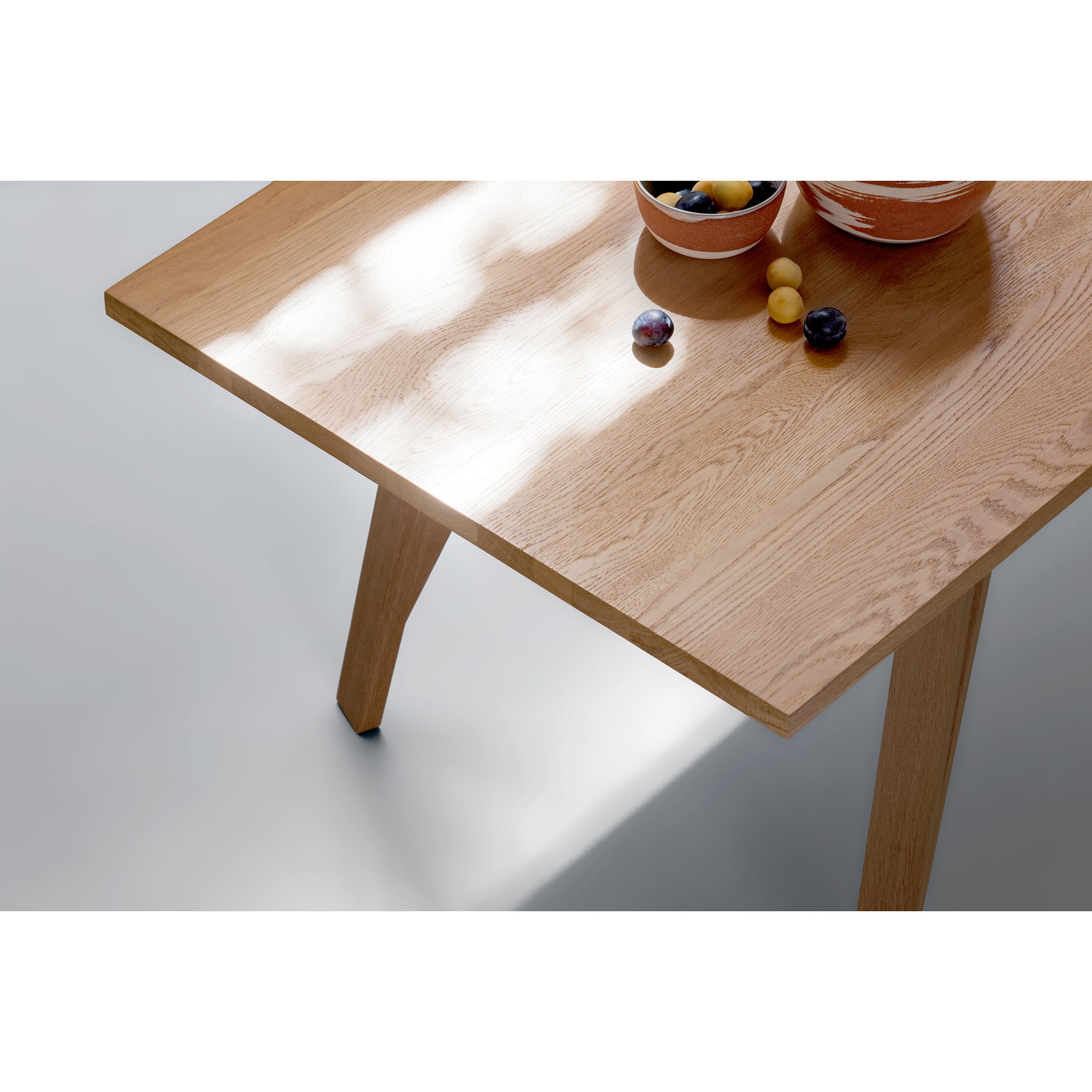 From above, the JL5 Sabeth Table by Loehr, crafted from solid oak with a smooth, glossy finish, is shown. A larger and smaller bowl of assorted fruits like grapes and plums rest on it. The tables elegant craftsmanship casts a soft shadow on the light-colored floor.