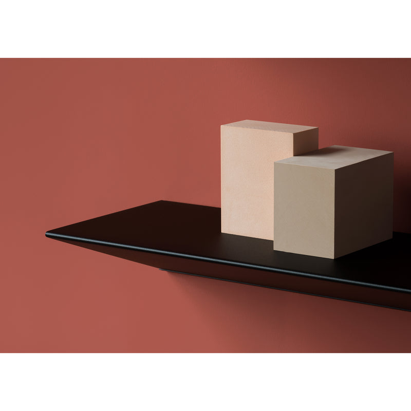 Two beige cubes rest on a Loehr L1 Newton Shelf with a triangular profile, made of sleek sheet steel, against a terracotta wall. With varying cube heights, the shelfs edge casts a distinct shadow, creating an inviting and uncluttered scene.