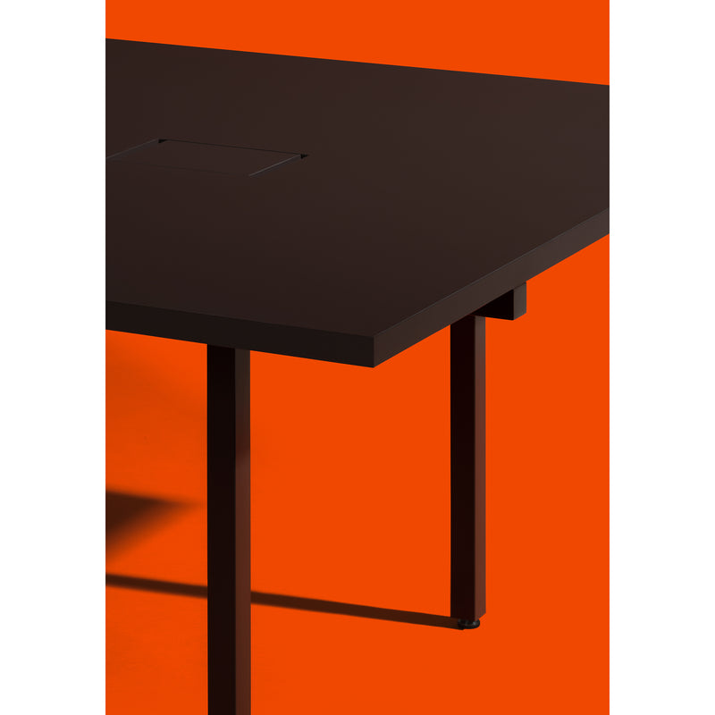 The L2 Eno Worktable by Loehr, featuring a sleek black design with angular legs, stands out against a vivid orange backdrop. Its minimalist design and sharp edges offer a striking contrast, making it an ideal hybrid workstation.