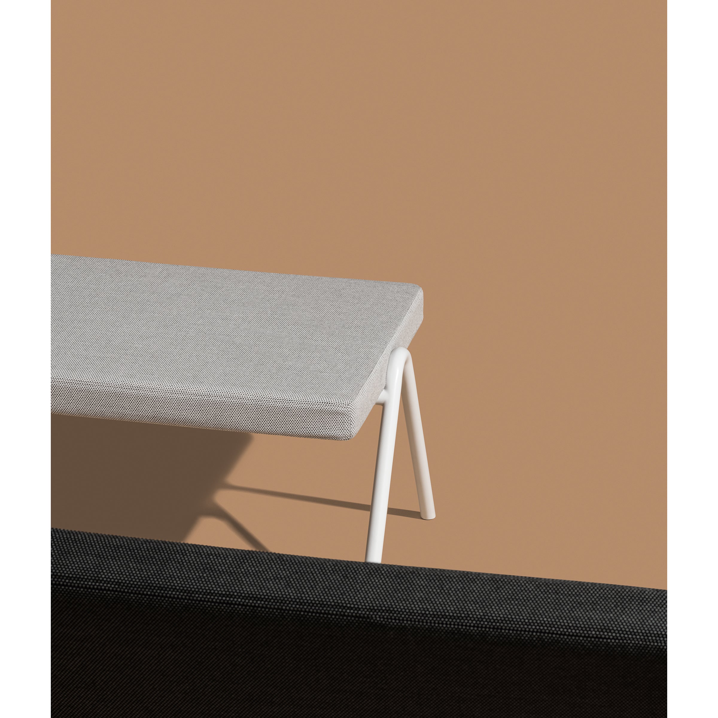 A minimalist image highlights the elegant DL6 Plato Bench by Loehr, featuring a gray rectangular seat with white V-shaped legs on a tan background. In the foreground, the backrest of a dark gray bench contrasts beautifully, epitomizing luxurious seating.