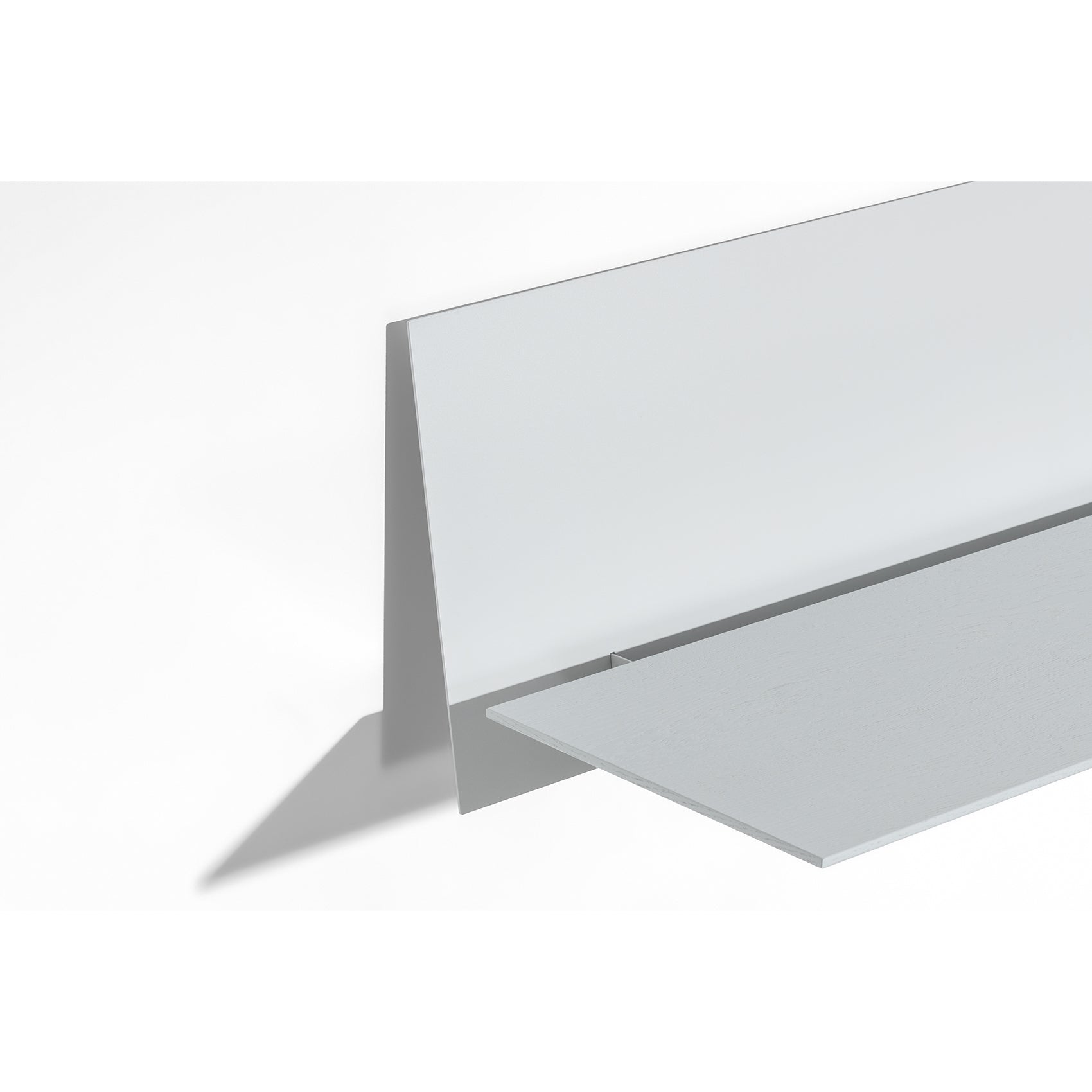 The S1 CHAPTER Bureau by Loehr features a minimalist, abstract design with geometric shapes forming an L-shaped structure casting shadows beside a fold-up tabletop. Its white and gray hues create a clean, modern aesthetic akin to sleek wall-mounted furniture.