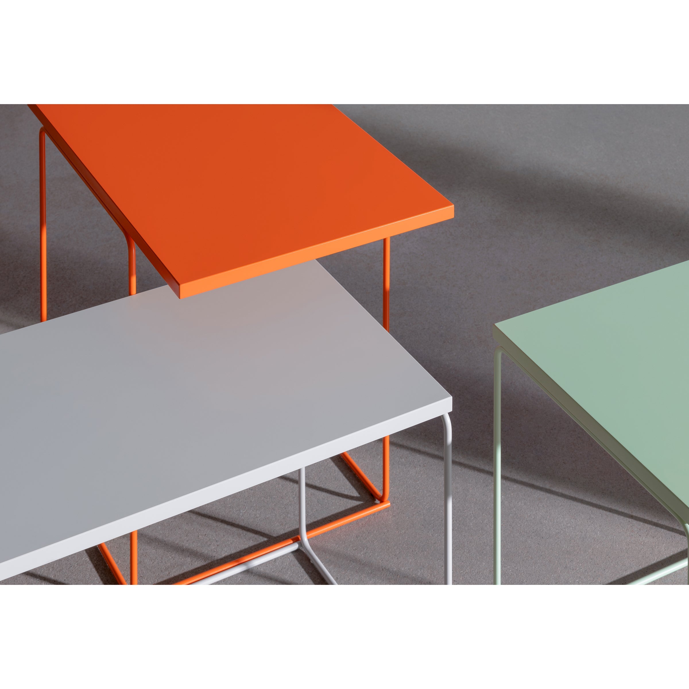 The DL1 Tangram Side Table Asymmetric by Loehr features three modern tables with slim metal legs overlapping in a geometric TANGRAM-inspired design. Vibrant orange, light gray, and soft green tops contrast against a neutral gray background, creating captivating shadows.