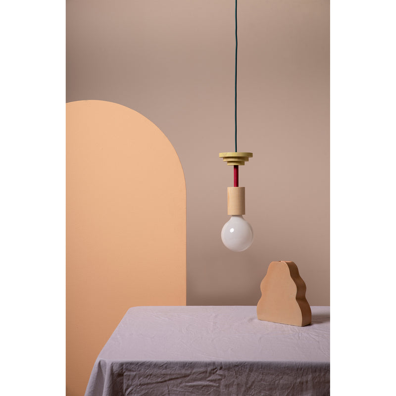 A minimalist room showcases Schneids Junit Mentis pendant lamp with a round bulb over a table with a white cloth. A curved, peach partition and an abstract clay sculpture add artistic flair to the beige background, enhanced by warm ash wood accents.