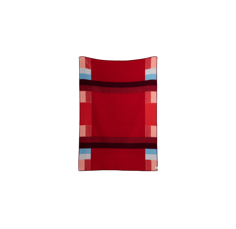 The Mikkel Large Throw by Roros is a red rectangular blanket made from soft Norwegian wool. It features Bauhaus-inspired geometric patterns in shades of pink, burgundy, and light blue with horizontal and vertical stripes forming a symmetrical block pattern.