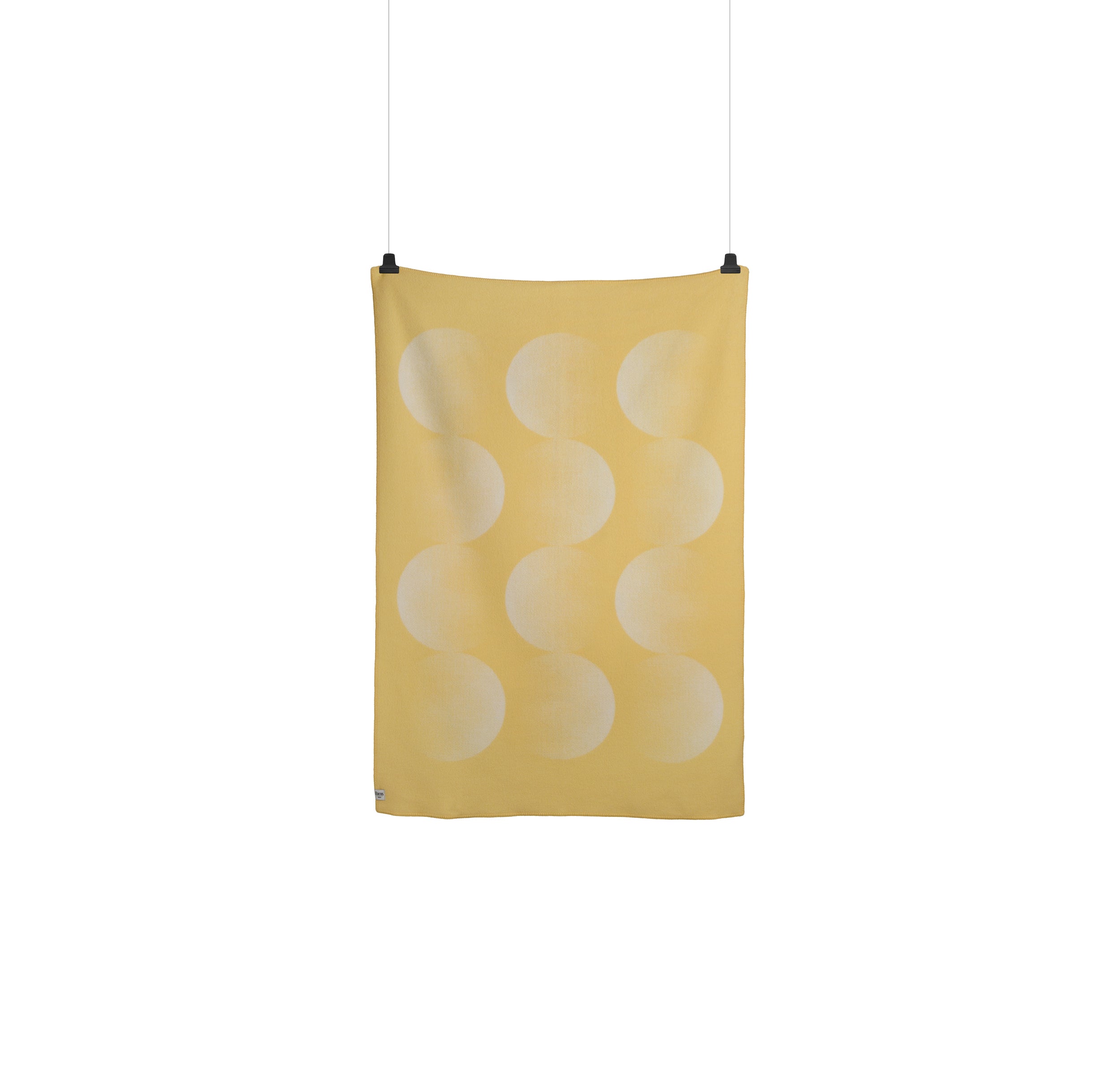 A yellow textile with overlapping faded white circles hangs vertically by two clips. Resembling the Moon Large Throw from Roros, it is smooth and embodies a minimalist, modern aesthetic reflective of Clara von Zweigbergks signature style.