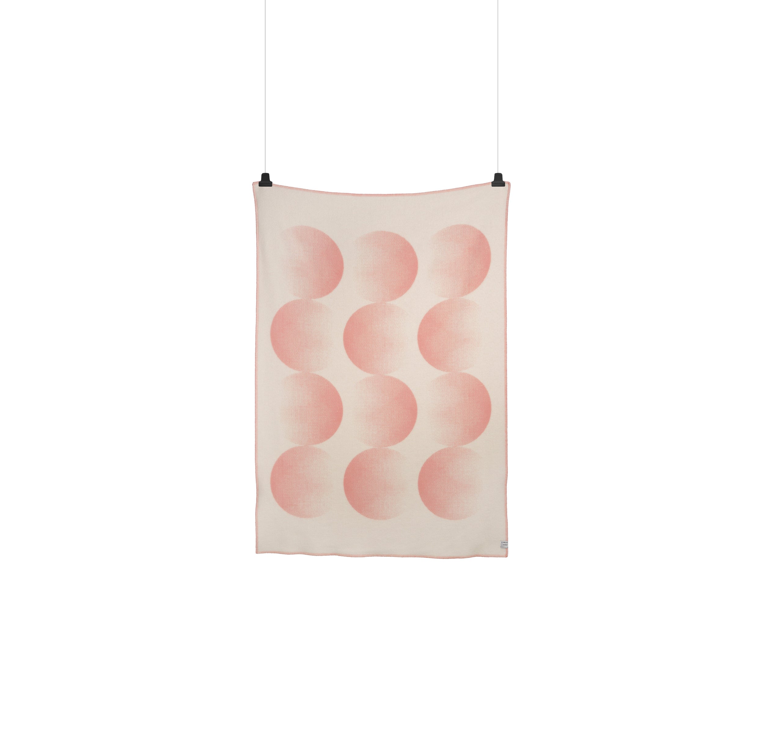 A Moon Large Throw by Roros, designed by Clara von Zweigbergk, hangs on the wall. Its pink crescents and semi-circles form four vertical columns on a light beige background, held up by visible clips.