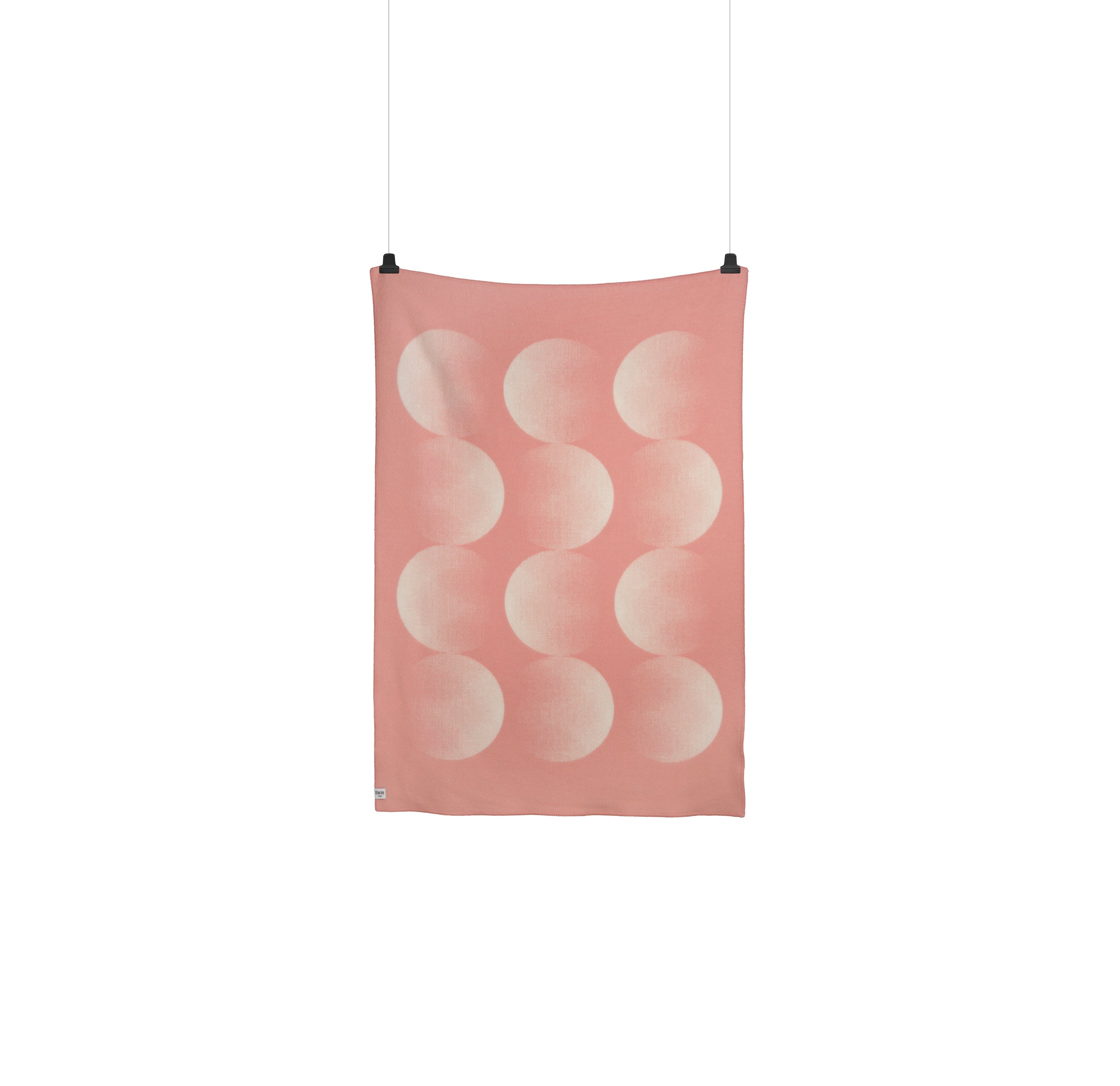 The Moon Large Throw by Roros drapes vertically, showcasing overlapping light-hued crescent shapes on pink fabric. Clipped at the top corners, it rests against a plain white backdrop, reflecting Clara von Zweigbergks unique design style.
