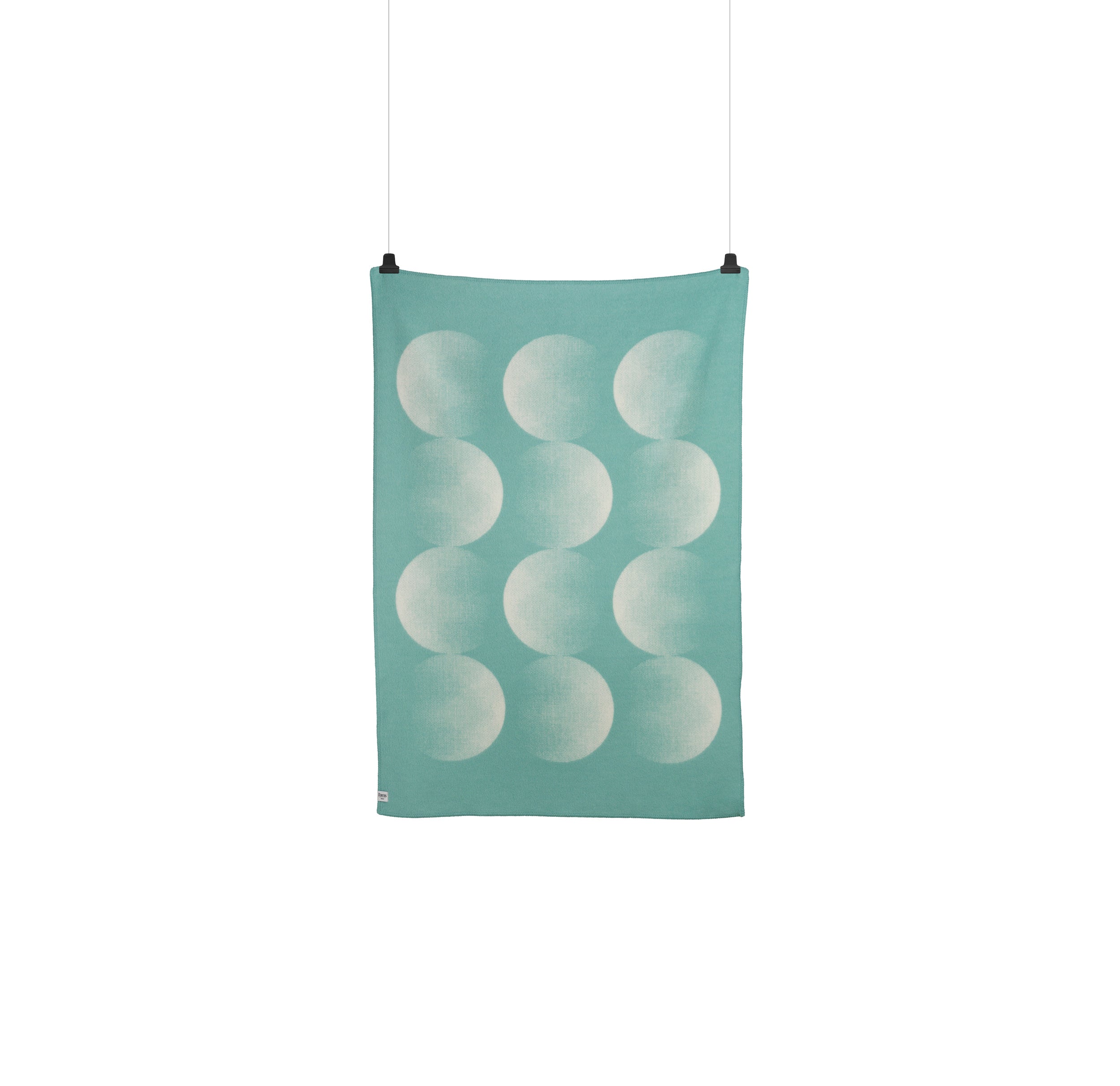 The Moon Large Throw by Roros is a hanging rectangular towel featuring a teal background with twelve crescent moons in a 3x4 grid. Reminiscent of Clara von Zweigbergks designs, it is clipped at the top and centered against a white background.