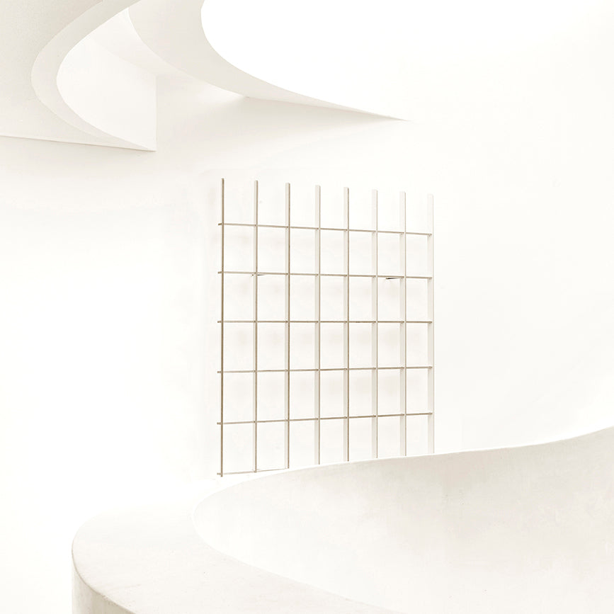 A minimalist architectural scene features Martin Breuer Bonos Open, a sleek bookcase with white curved walls and a grid-like design, creating clean lines and a soft, bright aesthetic.
