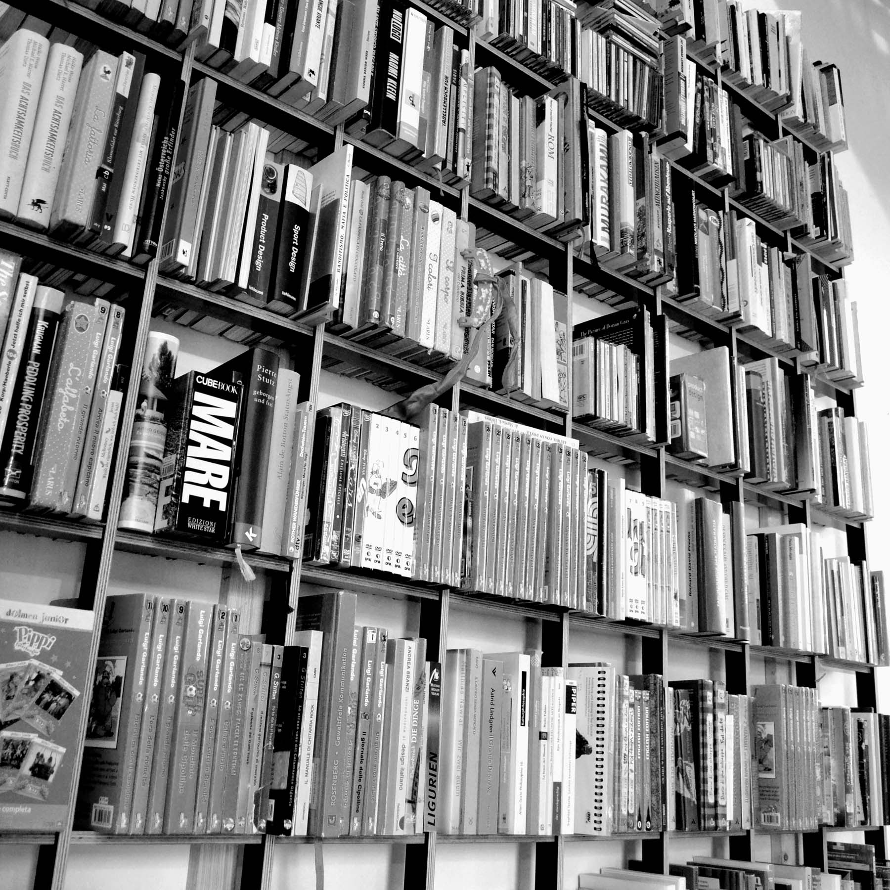 The SCHLAGSEITE bookshelf by Martin Breuer Bono is captured in a black and white photo, embodying minimalist design with its sleek vertical lines. Books arranged on its multiple shelves create a dense and visually striking sculptural pattern.