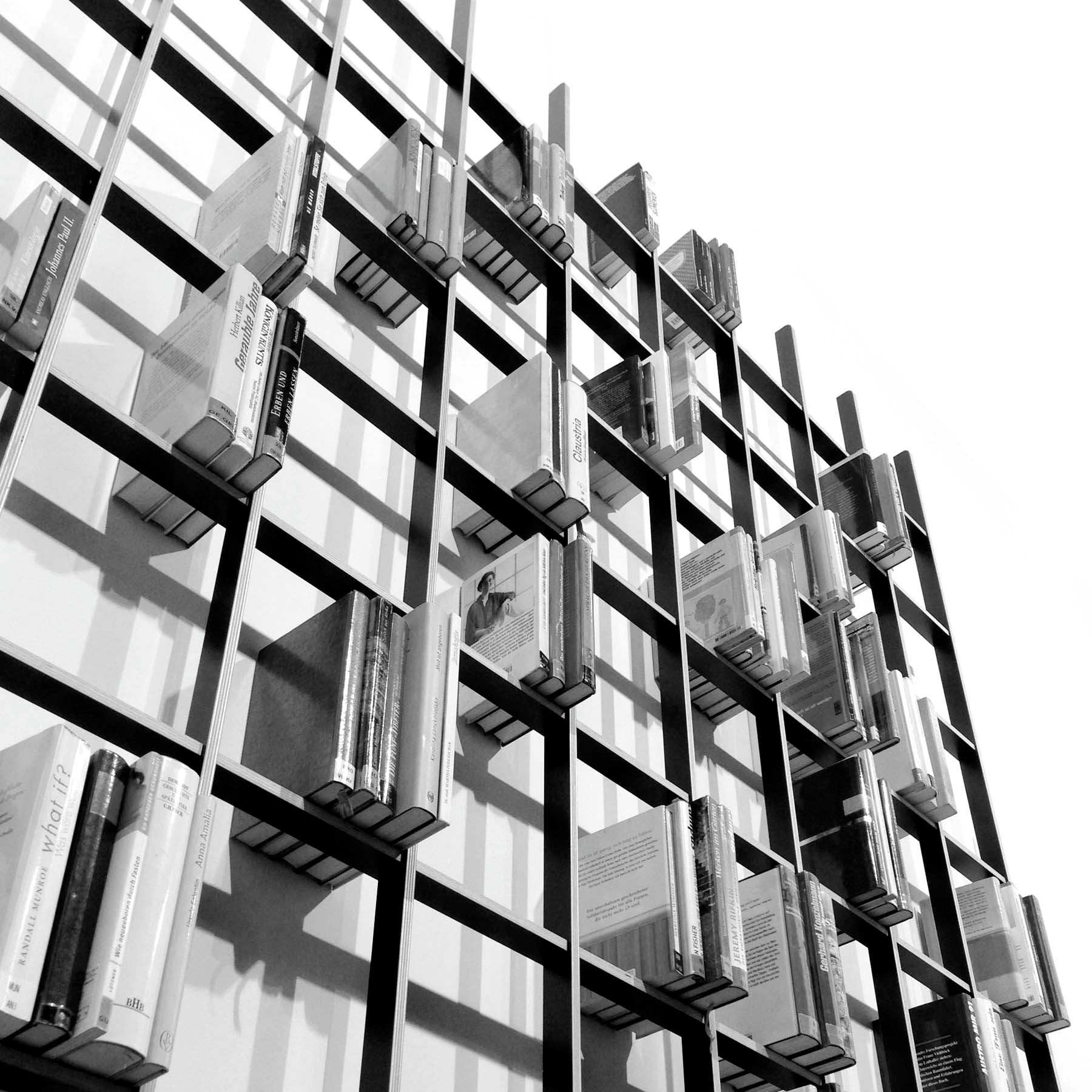 The SCHLAGSEITE bookshelf by Martin Breuer Bono features a black-and-white, grid-like design, showcasing books stacked in various orientations. Its sculptural form and geometric pattern embody the essence of minimalist furniture.