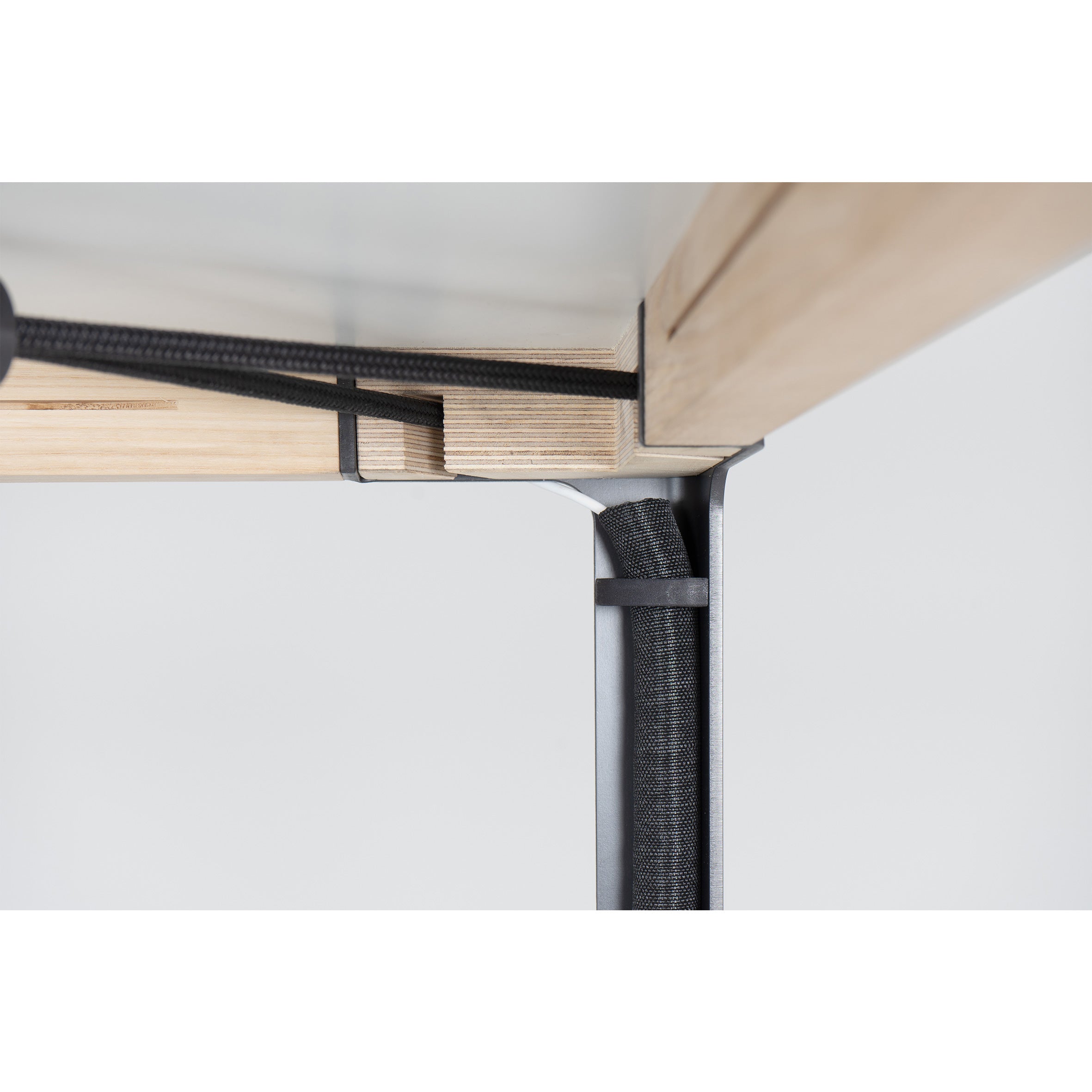 Close-up of the underside of a Moormann table highlights Cable Guidance, with magnetic brackets securing cables neatly to the wooden surface and metal frame for an organized design.