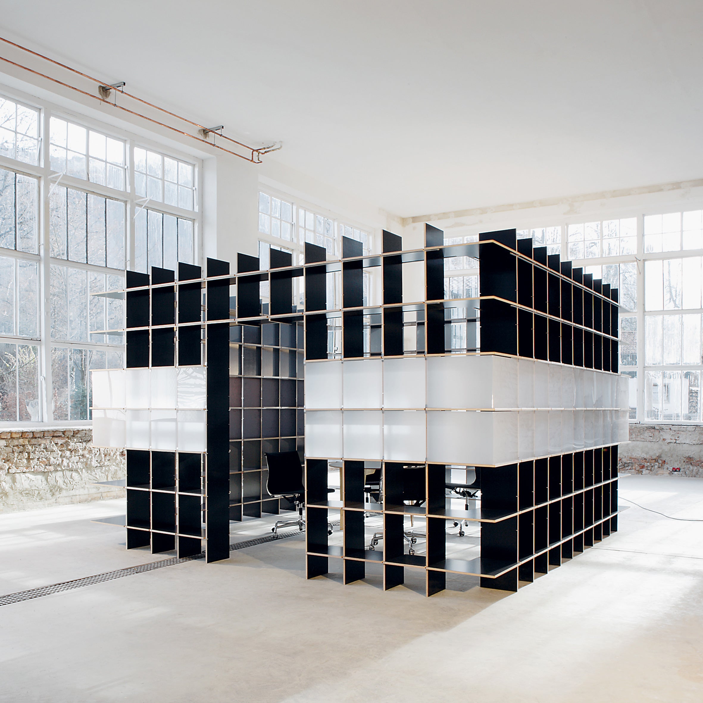 A modern office space featuring Moormanns FNP black and white grid structure is highlighted by an adaptable design, open ceilings, and large windows that brighten the minimalist area with chairs around a central desk, echoing Moormanns innovative style.