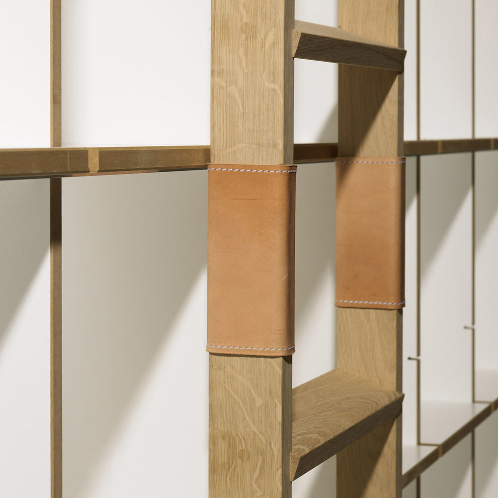 Close-up of Moormanns FNP wooden ladder with tan leather straps against a white wall. This minimalist design, inspired by Moormann, features rectangular rungs and vertical slats casting soft shadows, highlighting its adaptable design for seamless integration into any space.