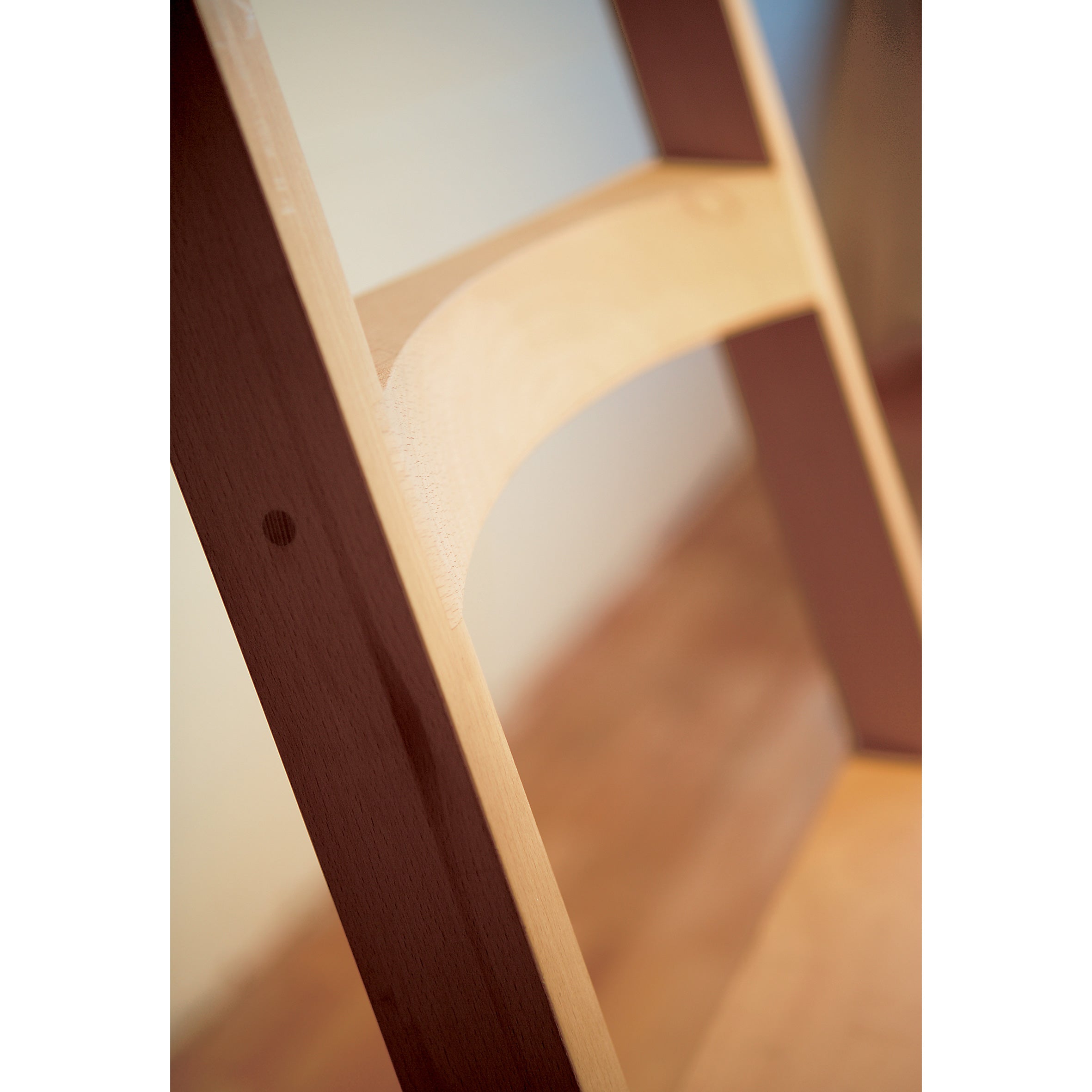 Close-up of the Moormann Hochacht, a wooden ladder-back chair crafted from untreated beech. It features two vertical supports with a curved horizontal slat and a seat with a light, smooth finish, reflecting the brands dedication to craftsmanship against a softly blurred background.