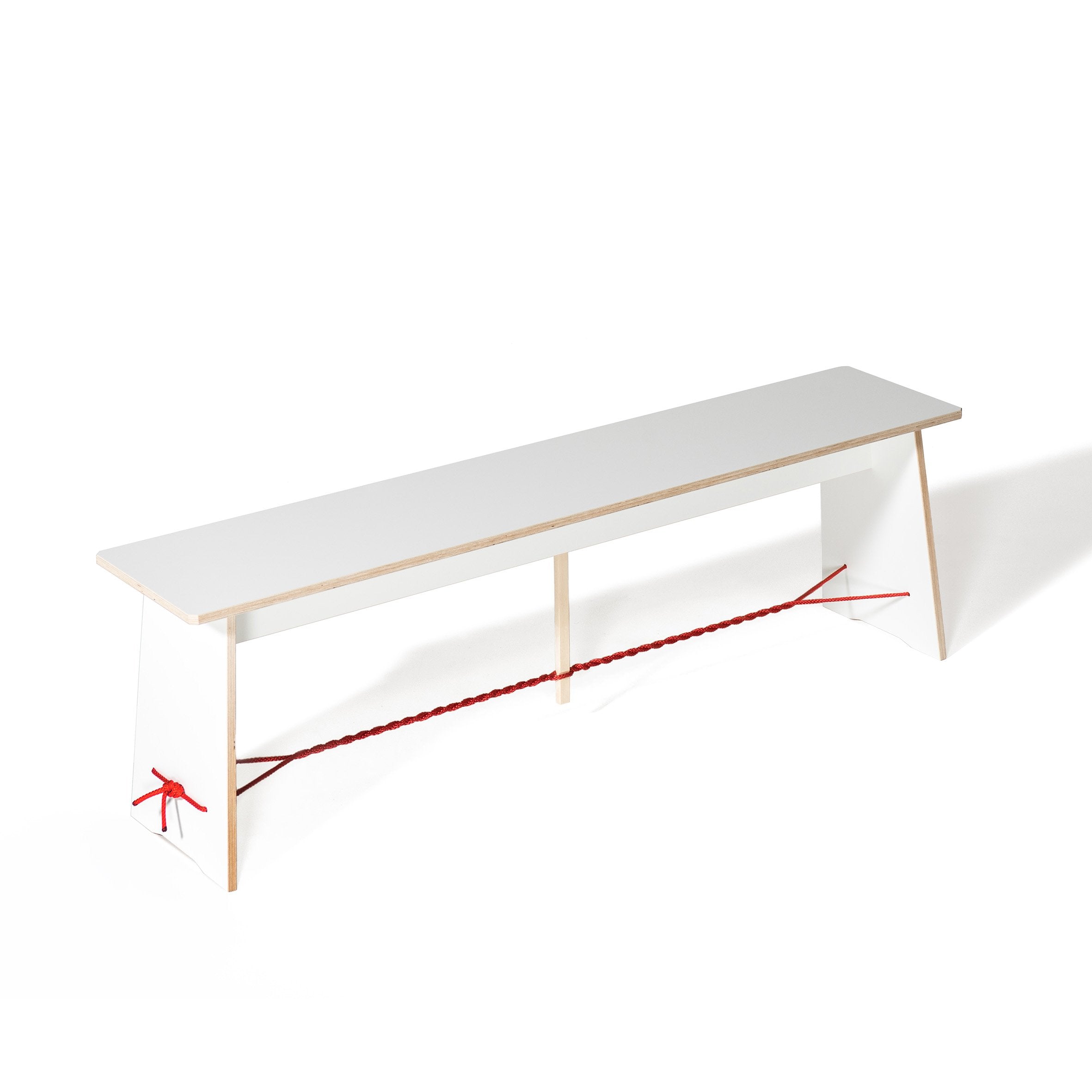 The Langer Max by Moormann is a minimalist white bench with angled legs for stability and is enhanced by a Strammer Max-like red rope interlaced between the legs, set against a plain white backdrop.