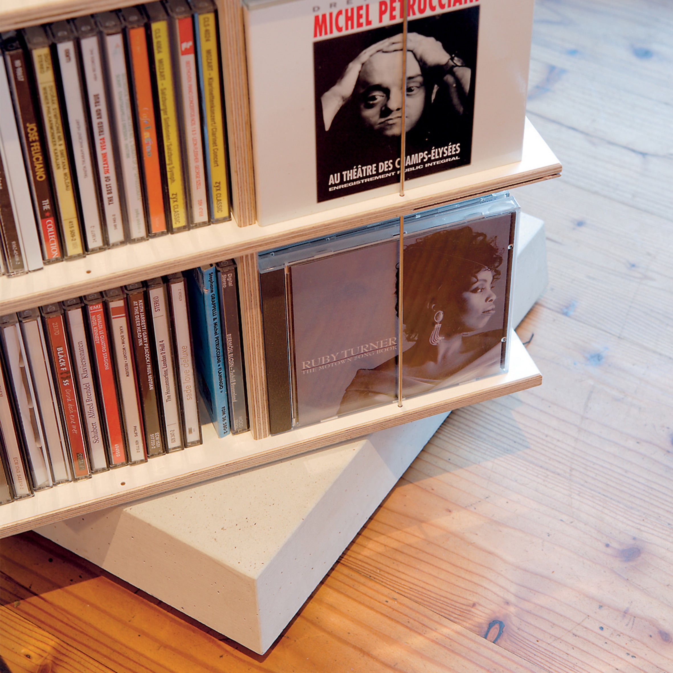 The Moormann Musikstapler, a rotatable CD rack, displays multiple CDs. One cover depicts a person in profile, another shows a musician with an instrument. This space-saving rack is set on a polished wooden floor.