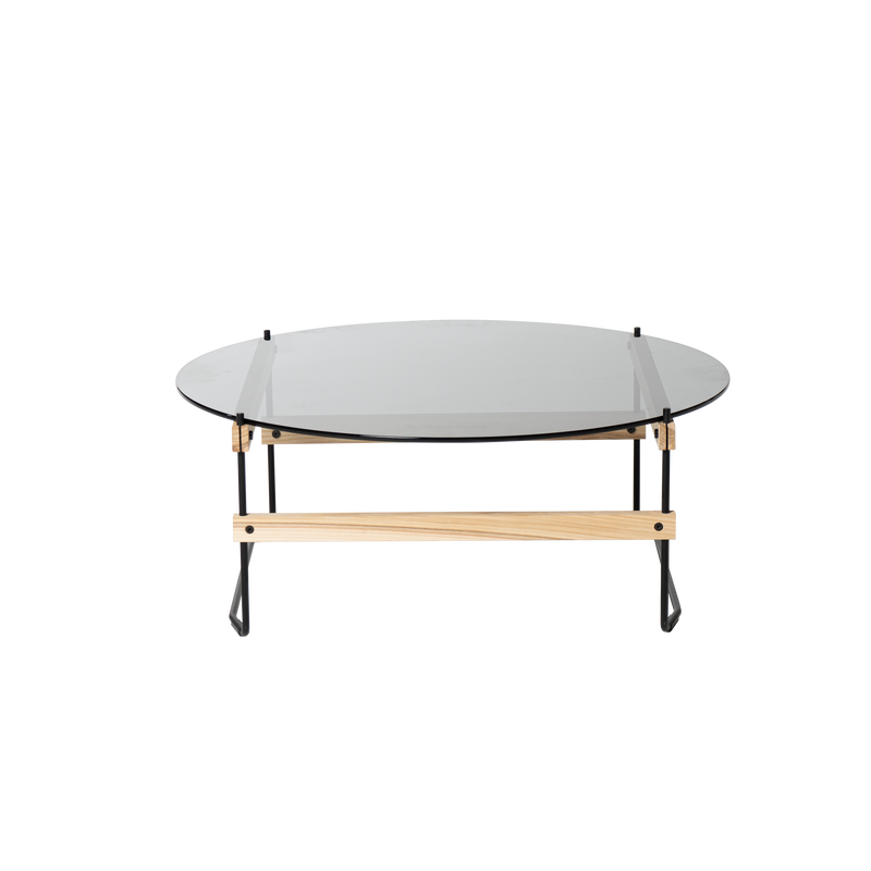 The Netto Coffee Table by Moormann features a sleek, round grey tinted ESG glass top, supported by a wooden frame and black metal legs—blending natural wood with industrial elements for a contemporary look.