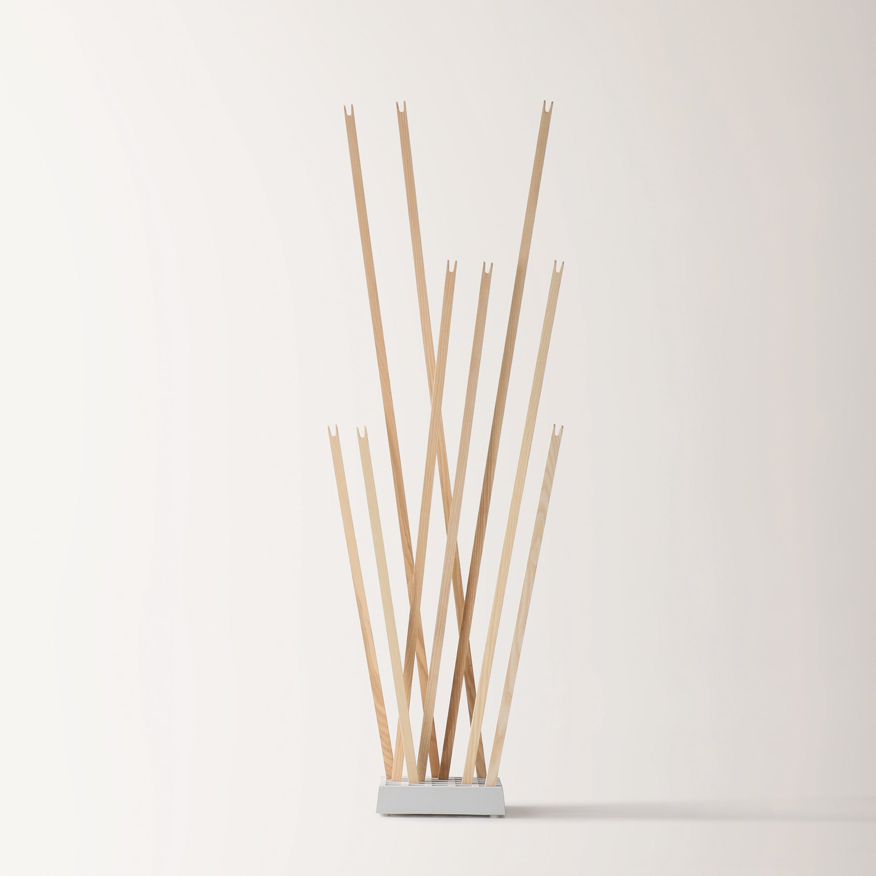 The Pin Coat by Moormann is a modern wooden coat rack with eight angled pegs on a rectangular white base, shown against a plain light backdrop.