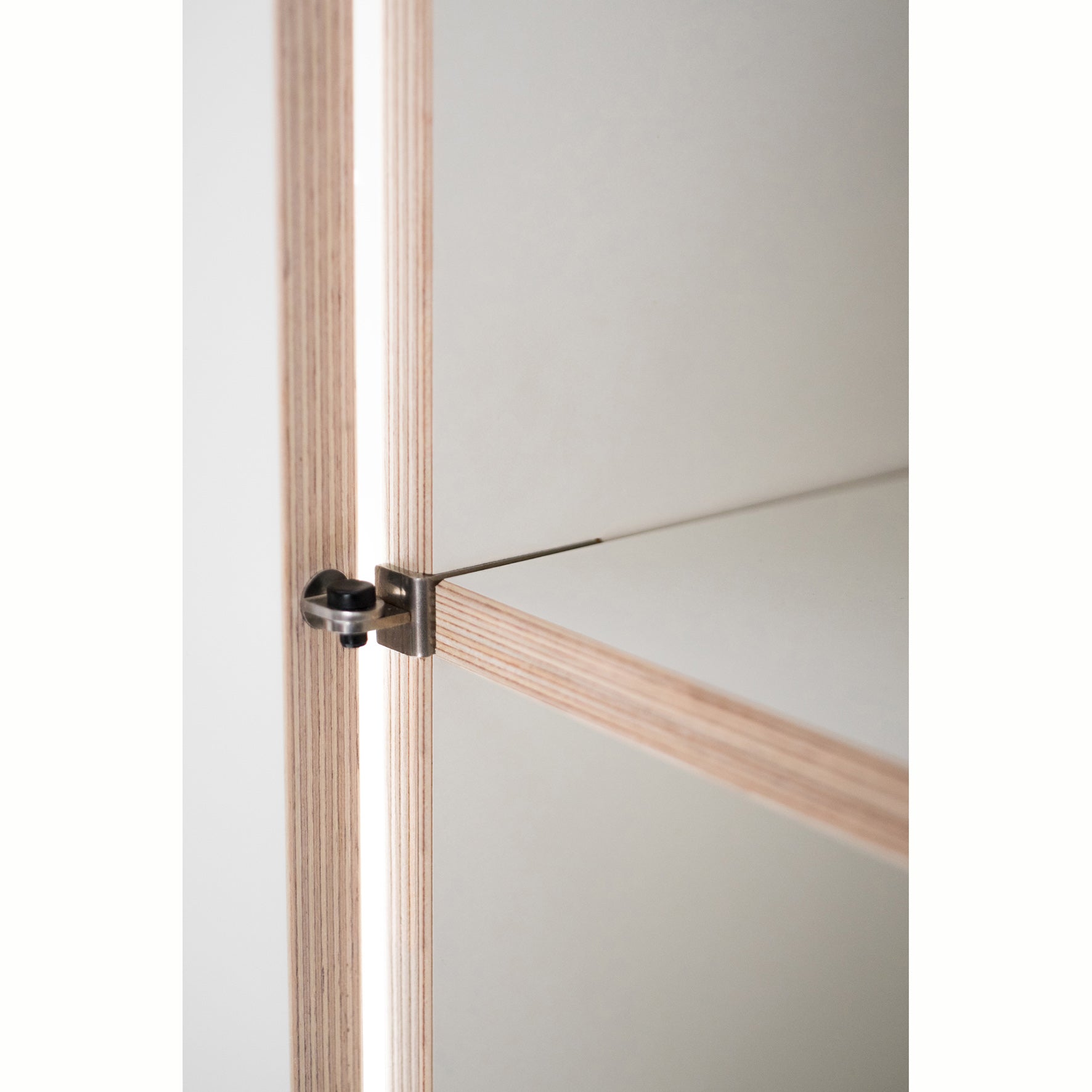 Close-up of a modern shelf corner from Moormanns Schrankone collection, featuring light wood edges and white surfaces. A metal connector joins vertical and horizontal panels, highlighting minimalist design and precise craftsmanship in this modular system.