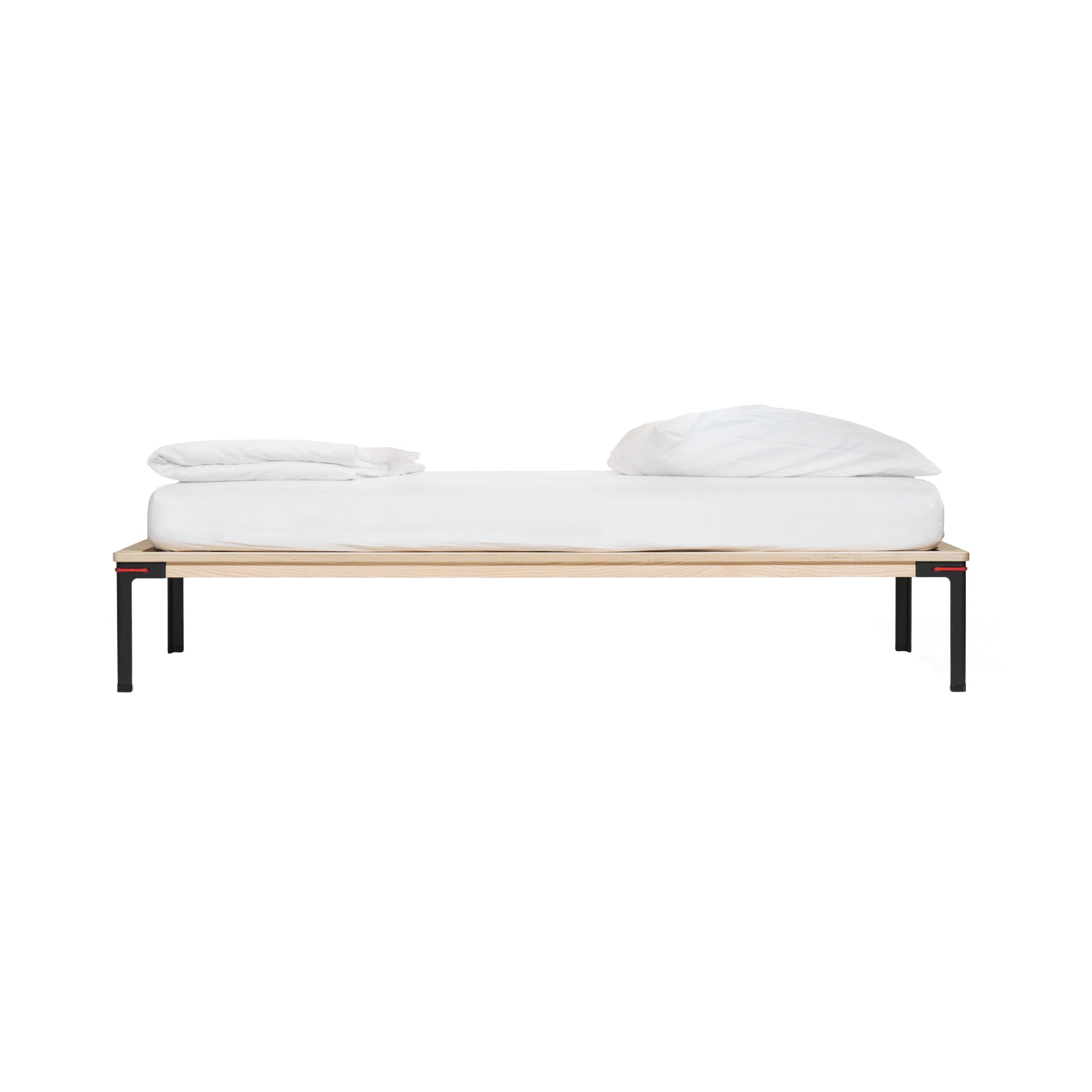 Side view of Moormanns Seiltänzer Bed showcasing a minimalist black frame and light wood base. A white mattress with two pillows sits atop the floating surface against a plain white backdrop.
