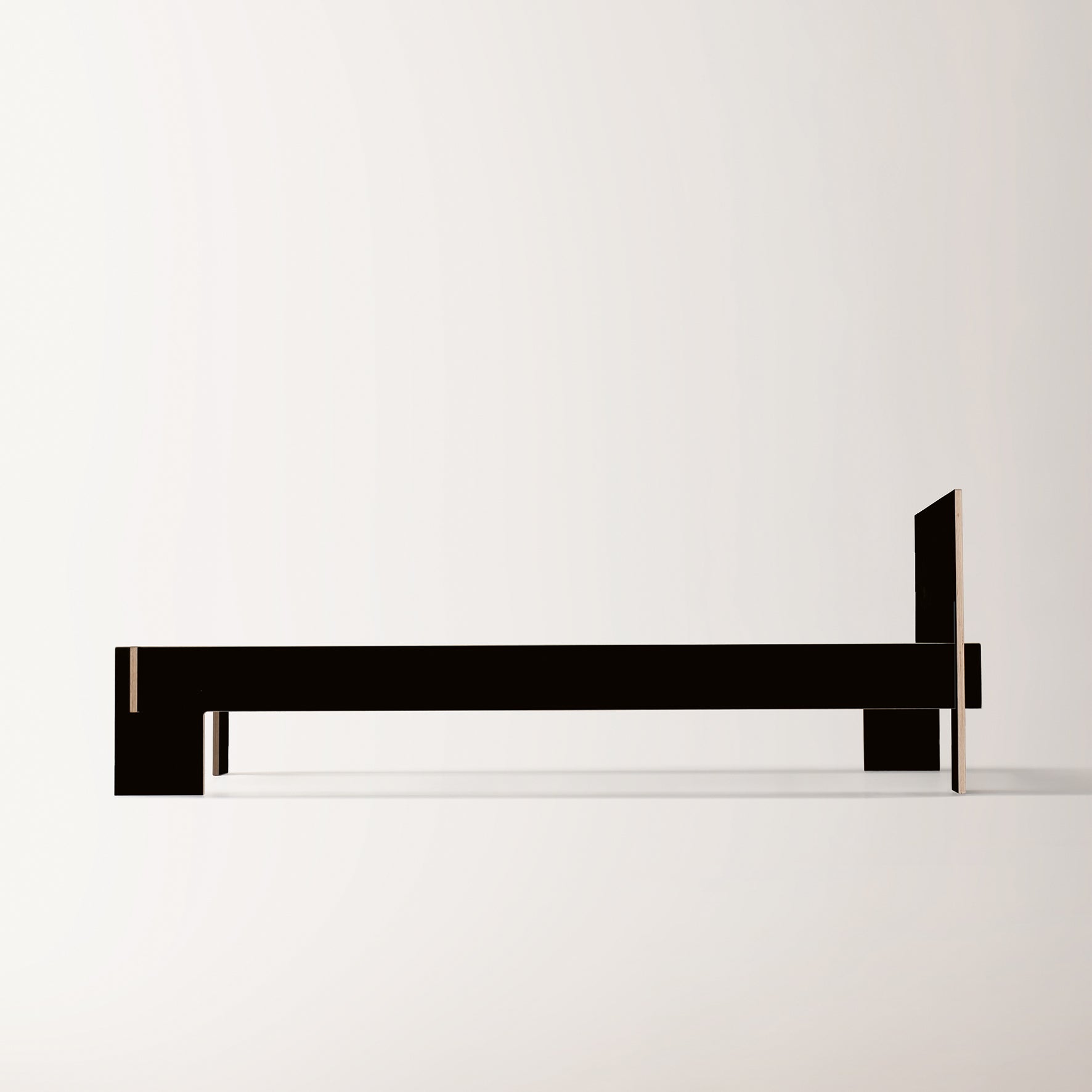 The Siebenschläfer bed frame by Moormann is a minimalist, modern piece crafted from birch plywood. It features clean lines in a dark hue against a light backdrop, with a headboard and geometric forms emphasizing elegance and contemporary style. Easy assembly requires no tools.