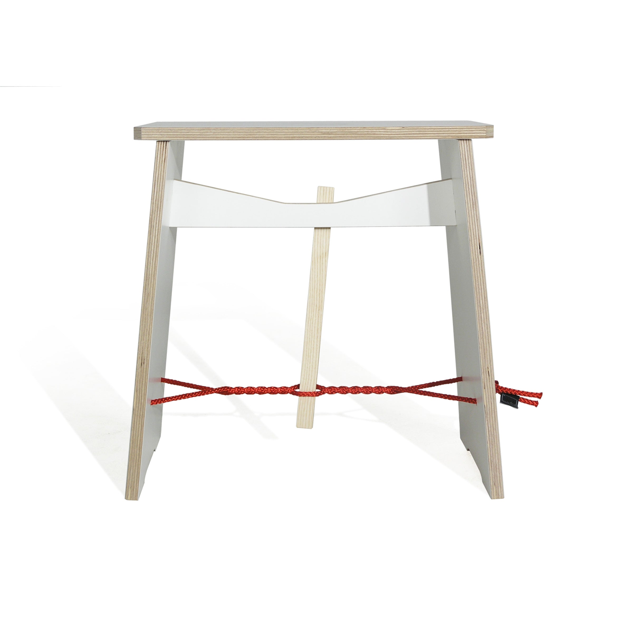 The Strammer Max by Moormann is a minimalist wooden stool made from birch plywood with a flat rectangular seat. Designed by Max Frommeld, it features two parallel legs connected by a red rope and a white horizontal bar, embodying simplicity and modernity.