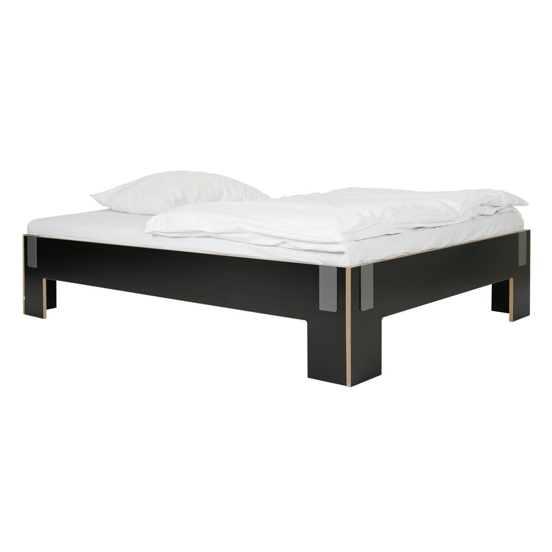 Moormanns Tagedieb bed features a sleek black frame with a modern low-profile design, complete with a neatly made white duvet and two white pillows. It includes metal corner accents and an adjustable mattress support for enhanced comfort.